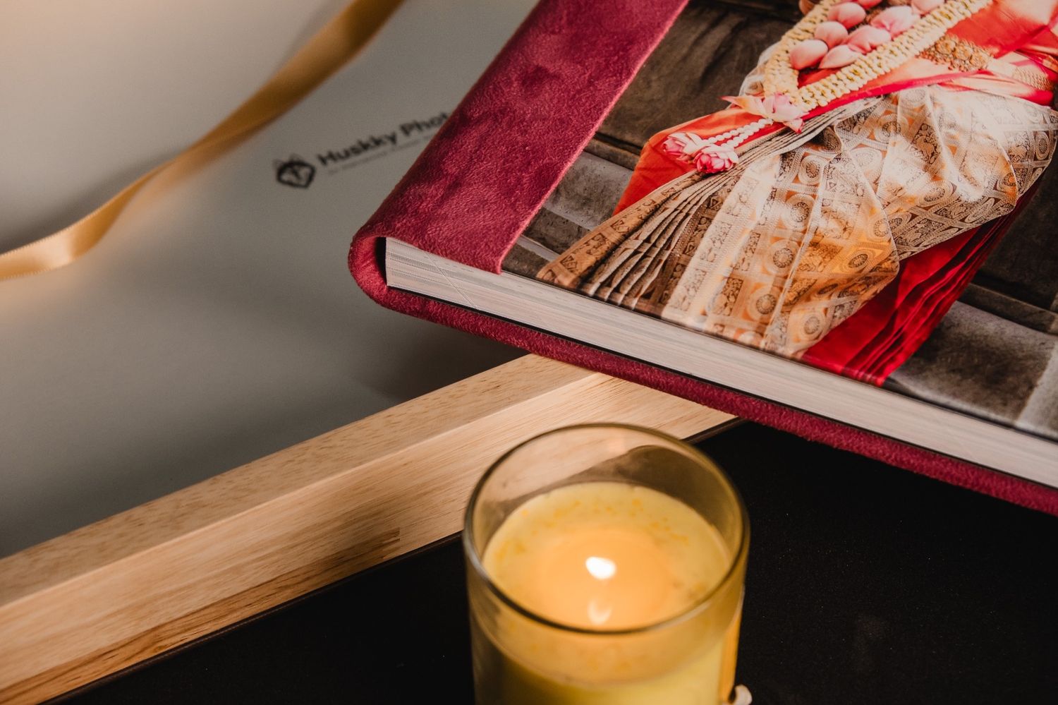 A lit candle in a glass jar beside a wedding photo album on a wooden shelf.