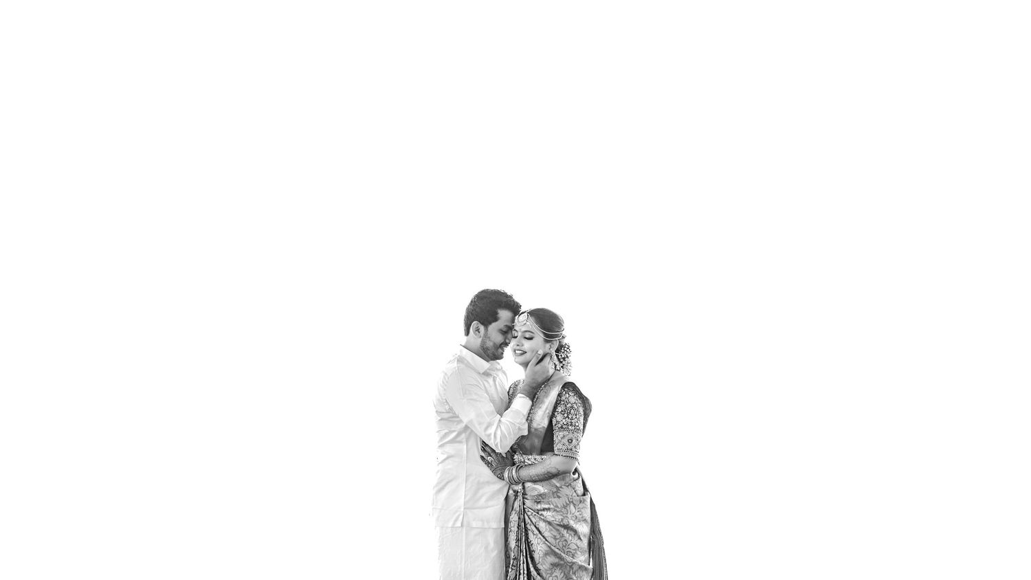 Black and white photo of an elegant couple in traditional Indian attire sharing a romantic moment.