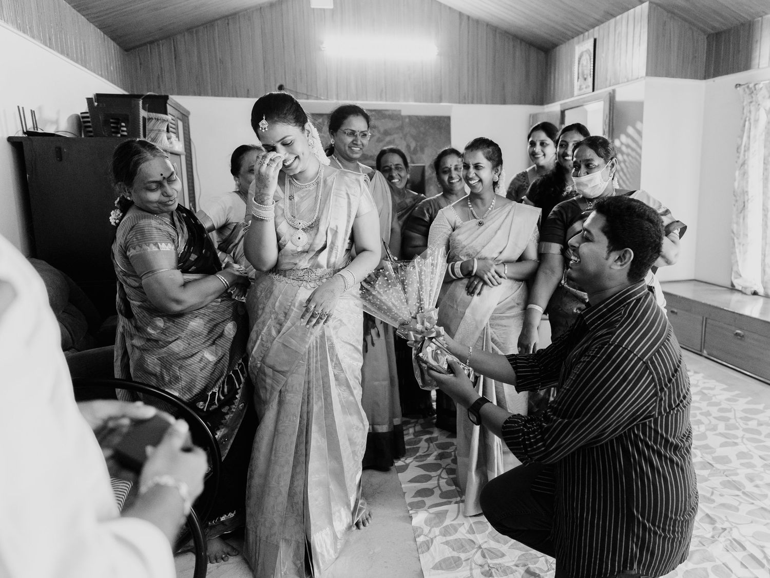 Black and white photo of a South Indian wedding ceremony with women in sarees gathered around an emotional bride.