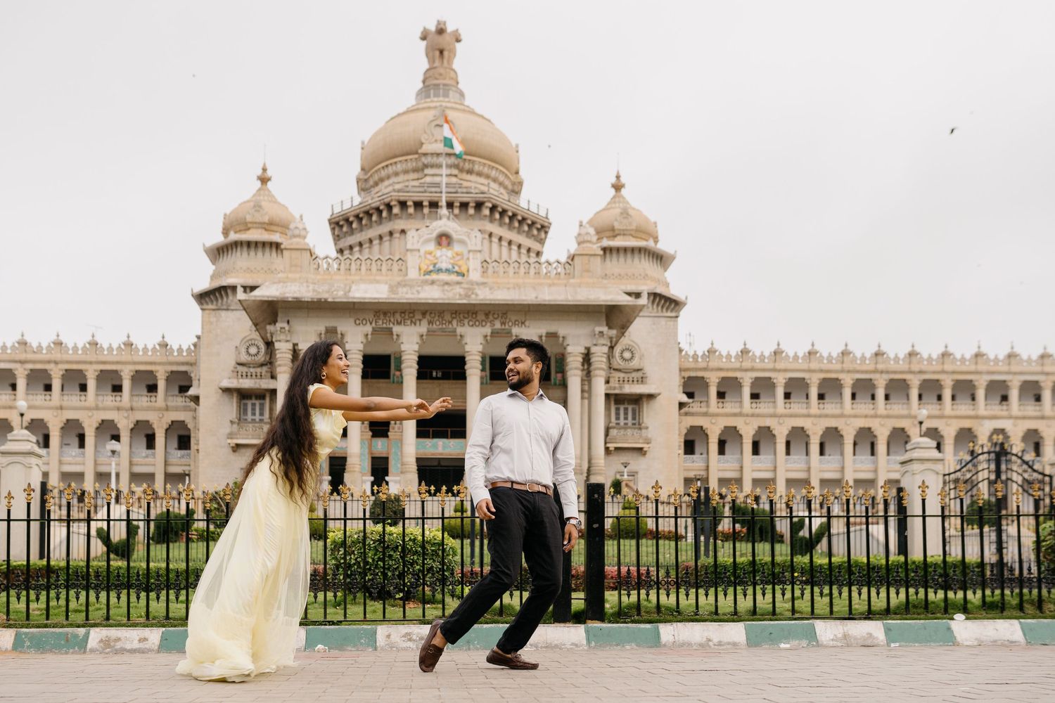 Couple dancing in front of Vidhana Soudha in Bangalore, India, wearing elegant attire for a pre-wedding shoot.