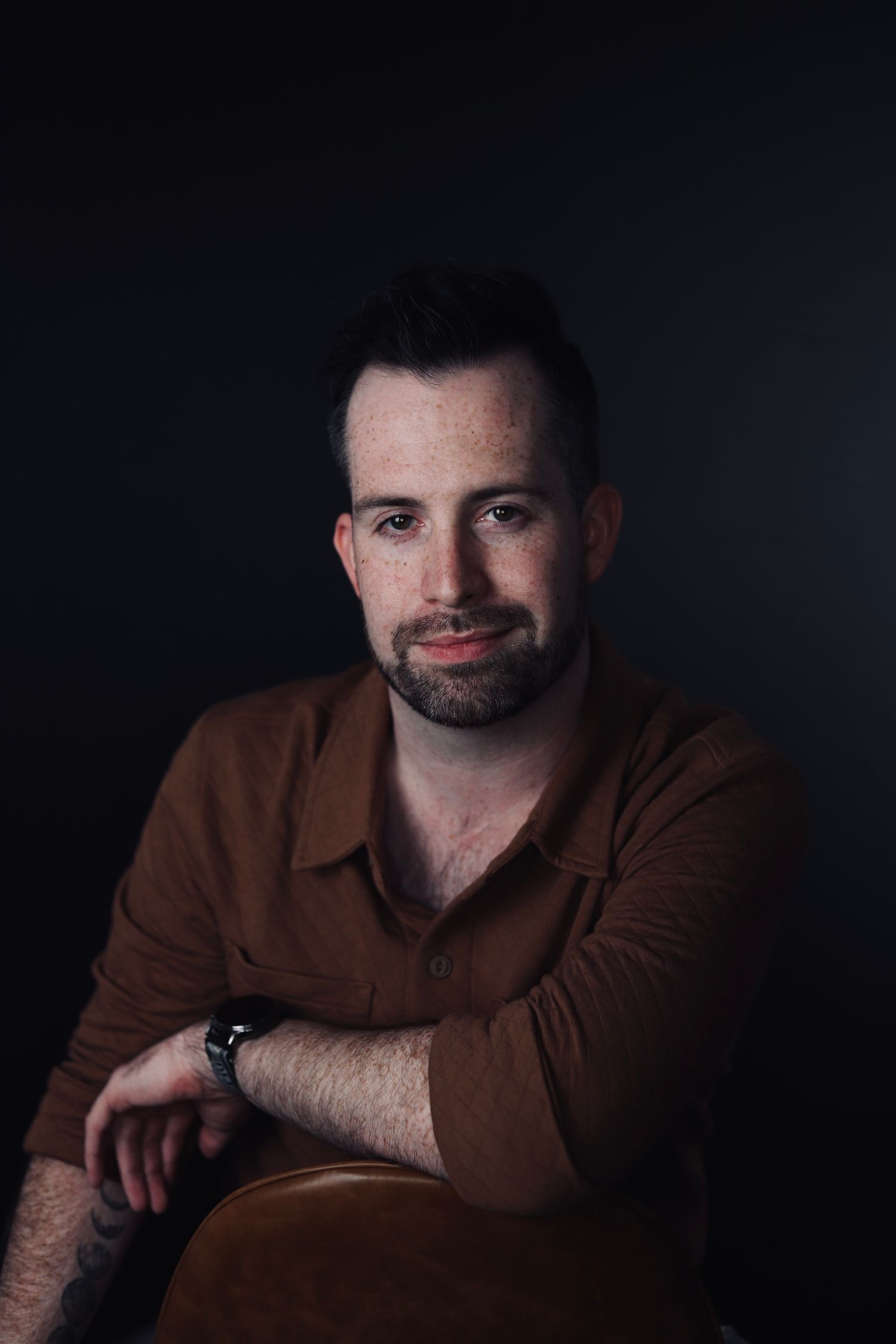 Moody portrait of a person wearing a brown sweater in dramatic lighting.