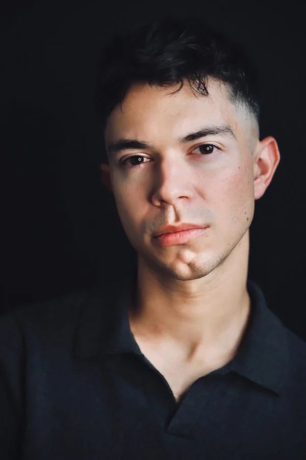 Dramatic portrait in dark polo shirt against black background.