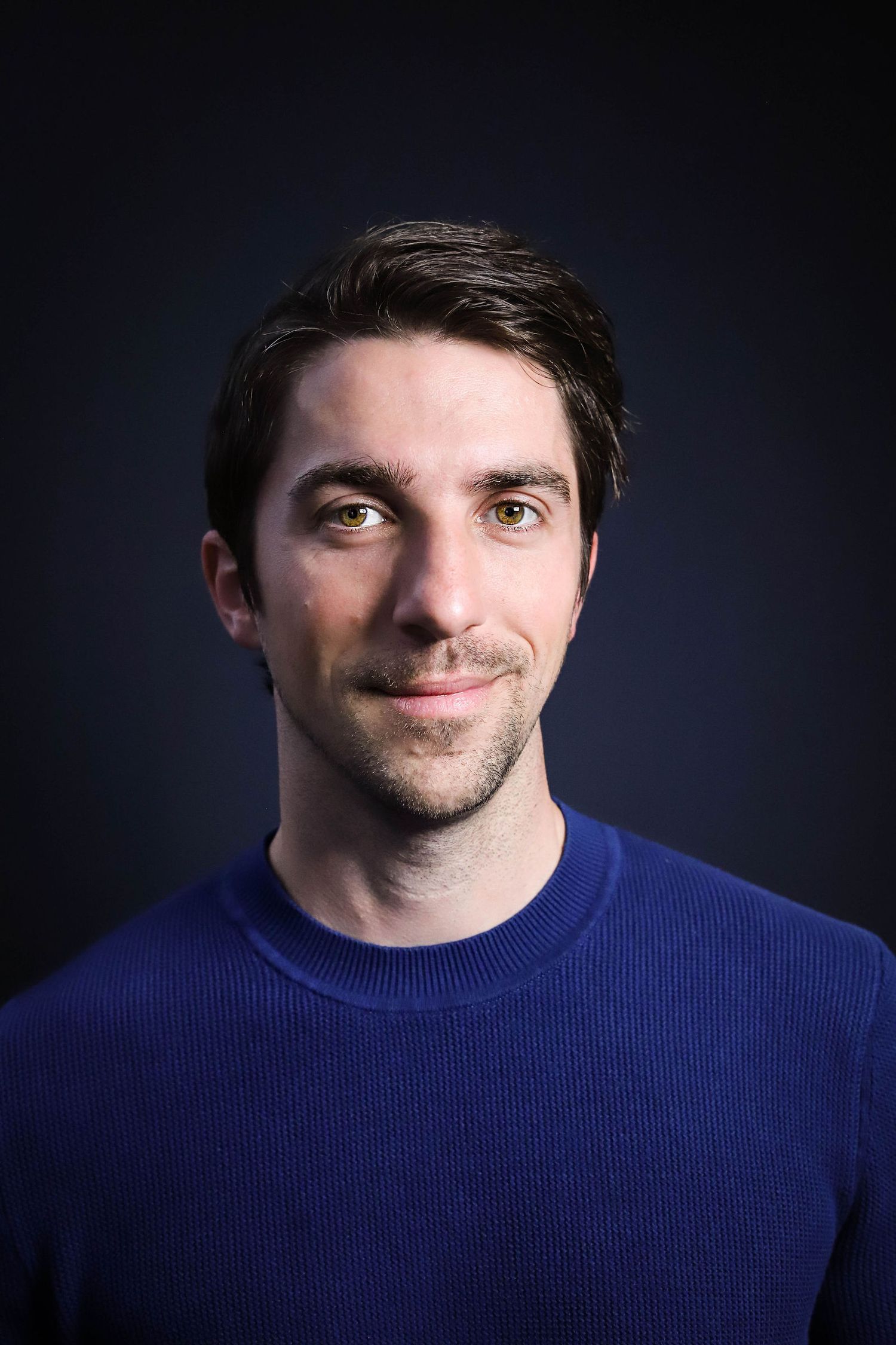 A series of headshots featuring someone wearing a royal blue sweater against a dark studio backdrop.