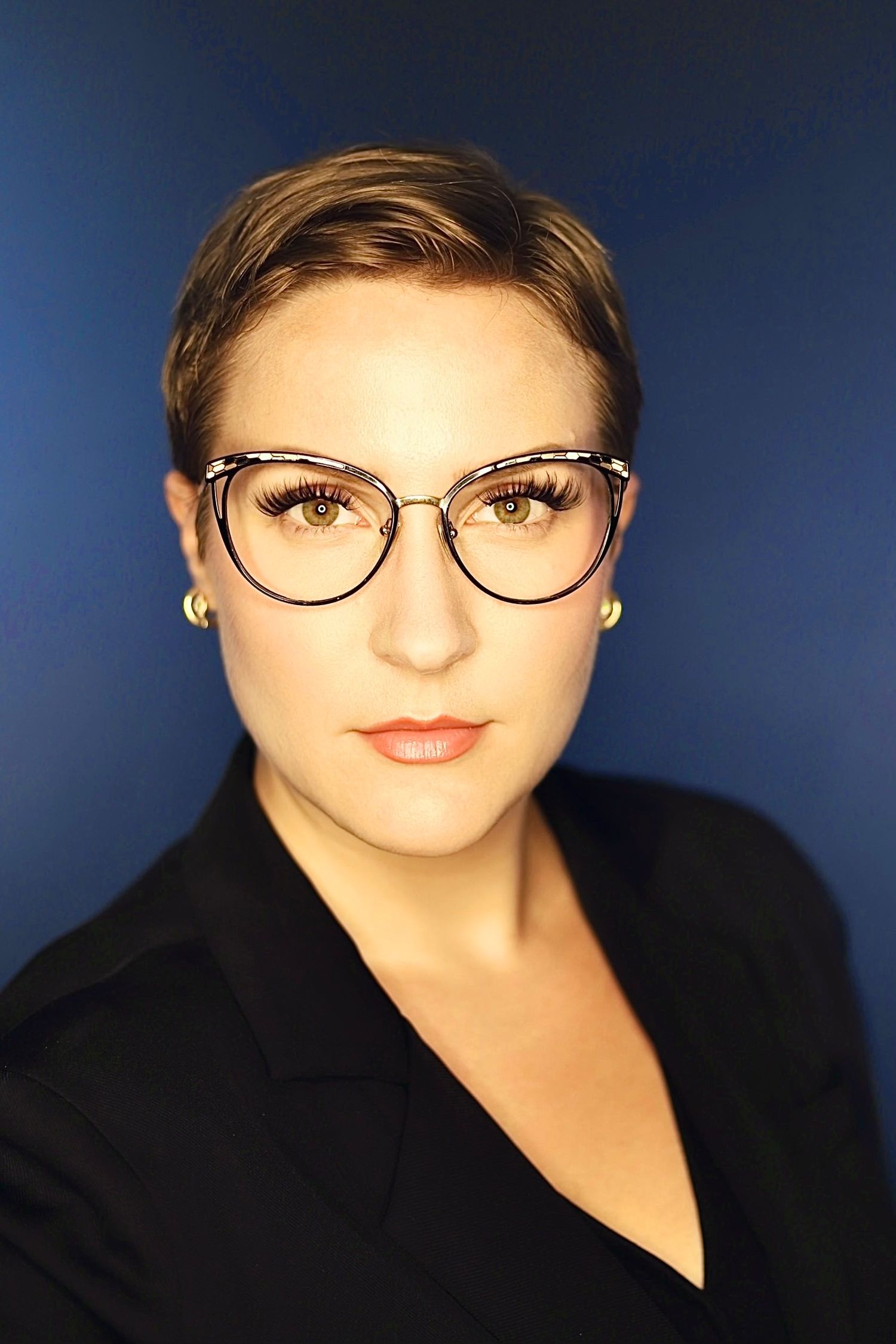 Professional headshots featuring black blazer and round glasses against blue backdrop.