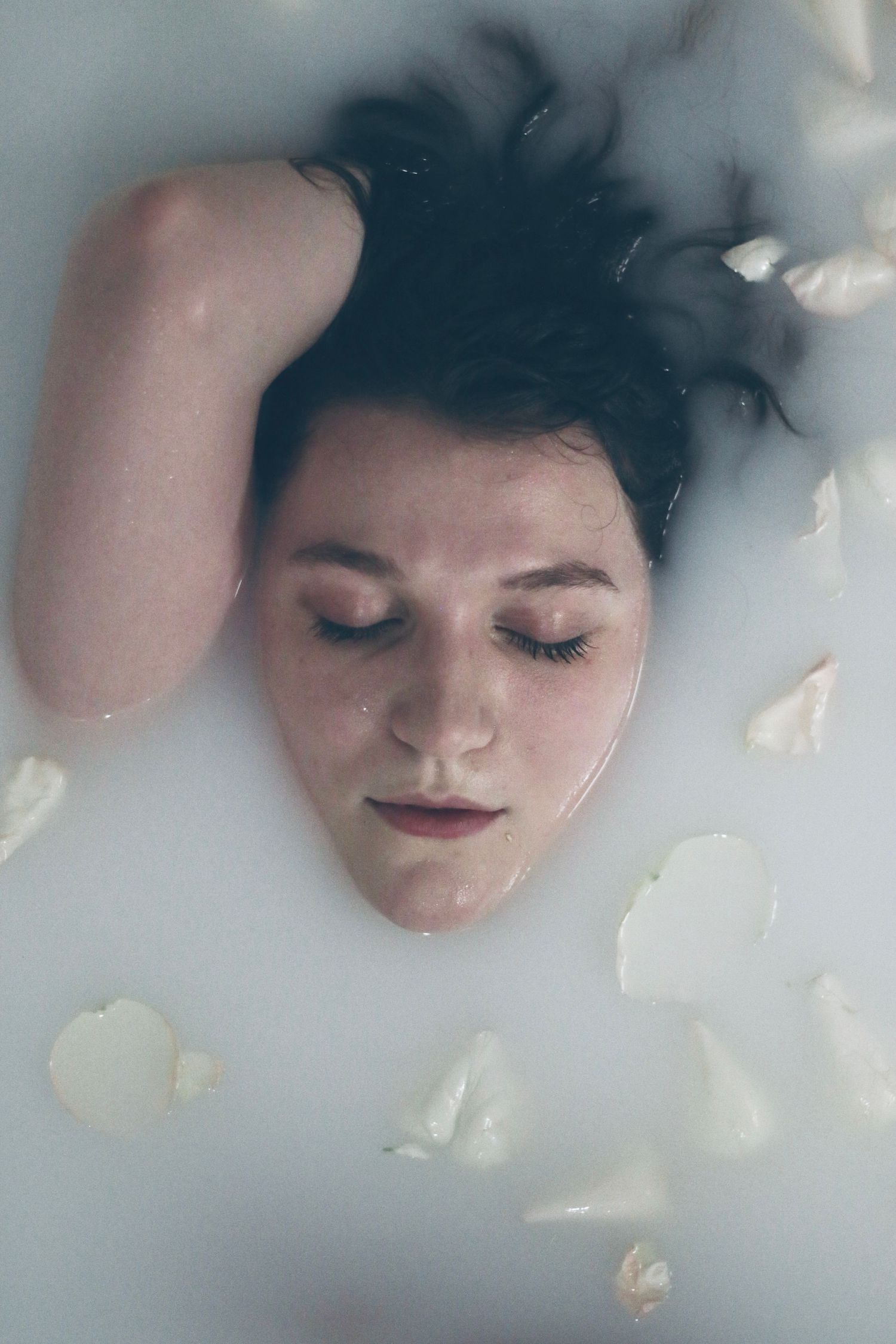 Dreamy portrait in milk bath with rose petals and soft lighting.