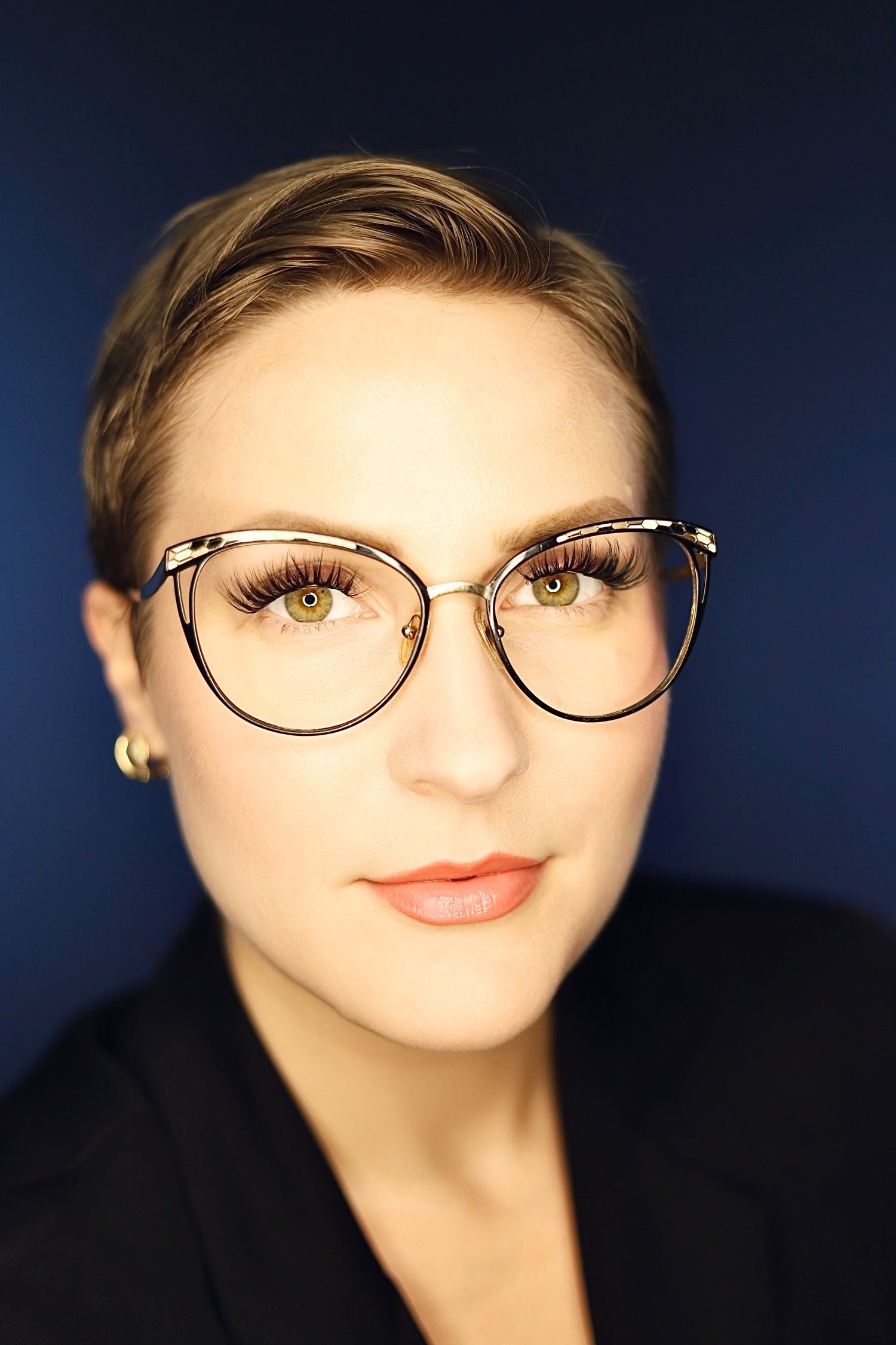 Close-up portraits with wire-frame glasses and coral lipstick against navy background.