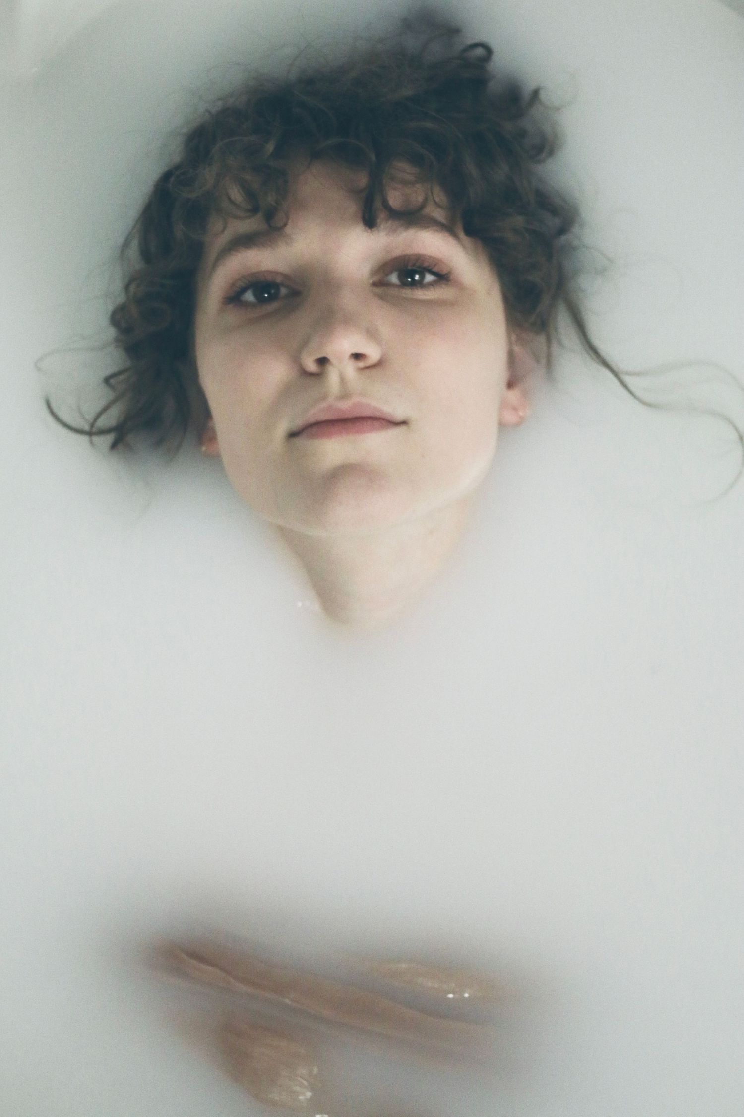Artistic portrait with curly hair in misty white setting and soft lighting.