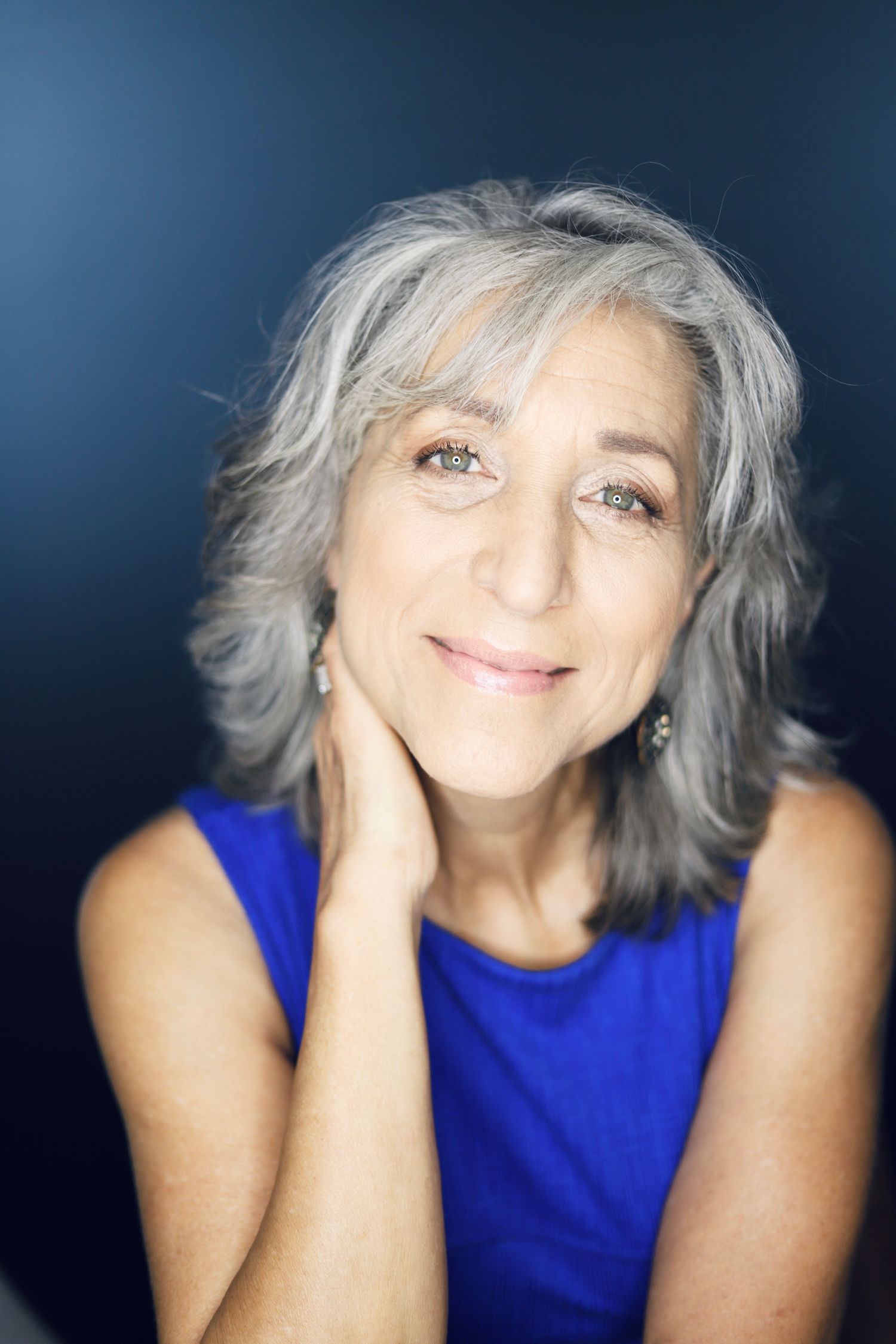 Warm portrait in vibrant blue sleeveless top against dark background.