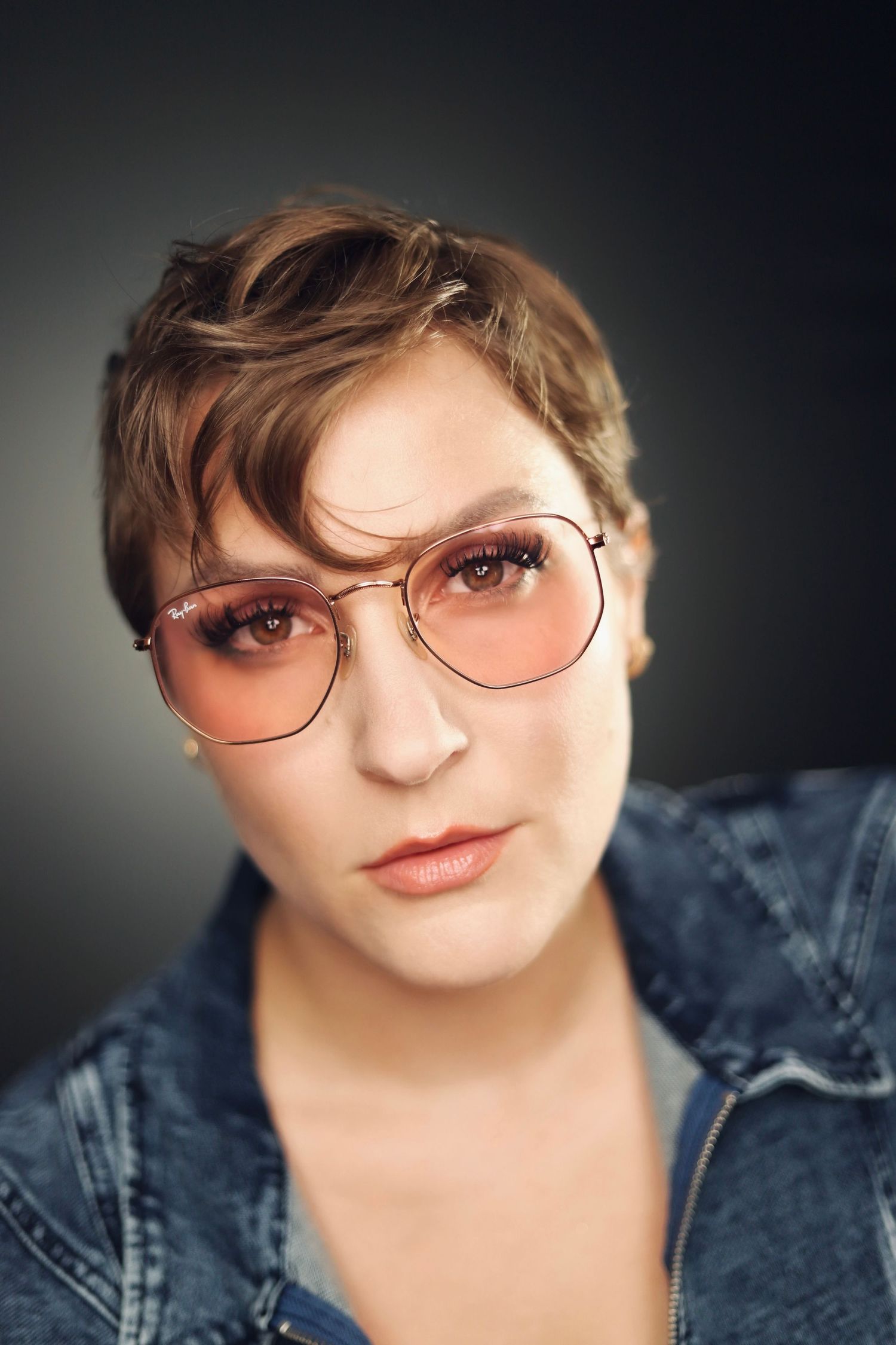 Professional portrait in denim jacket and glasses with dramatic lighting and soft makeup.
