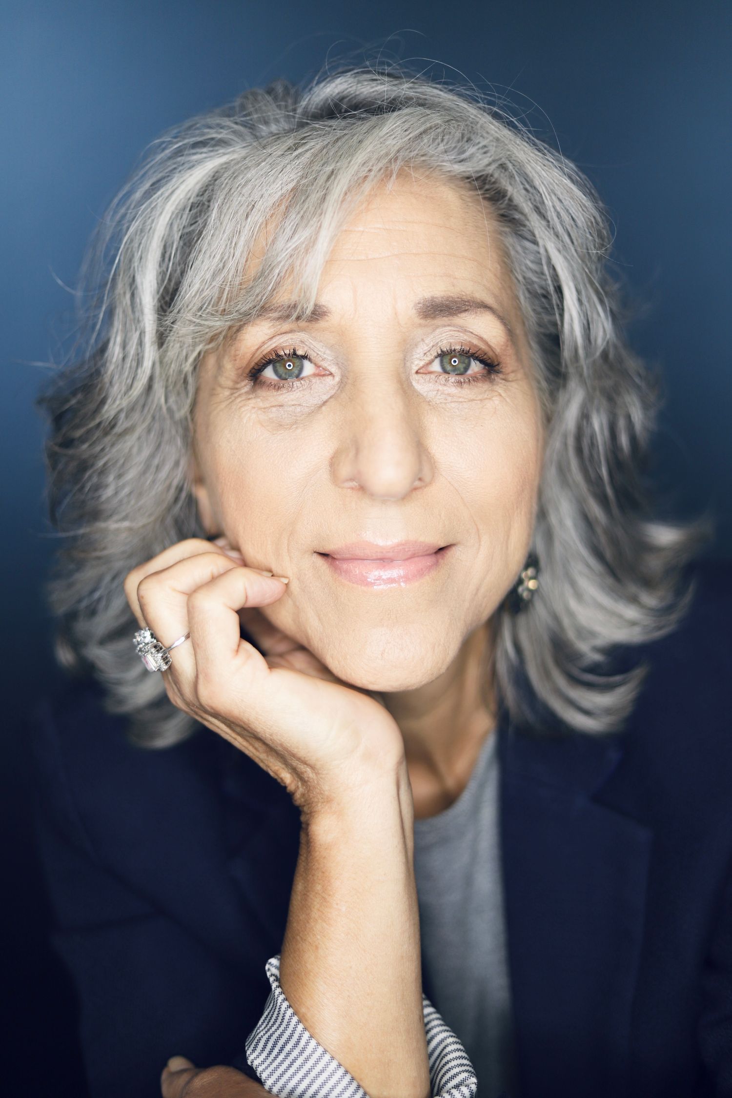 Elegant portrait with hand resting on chin against blue background.