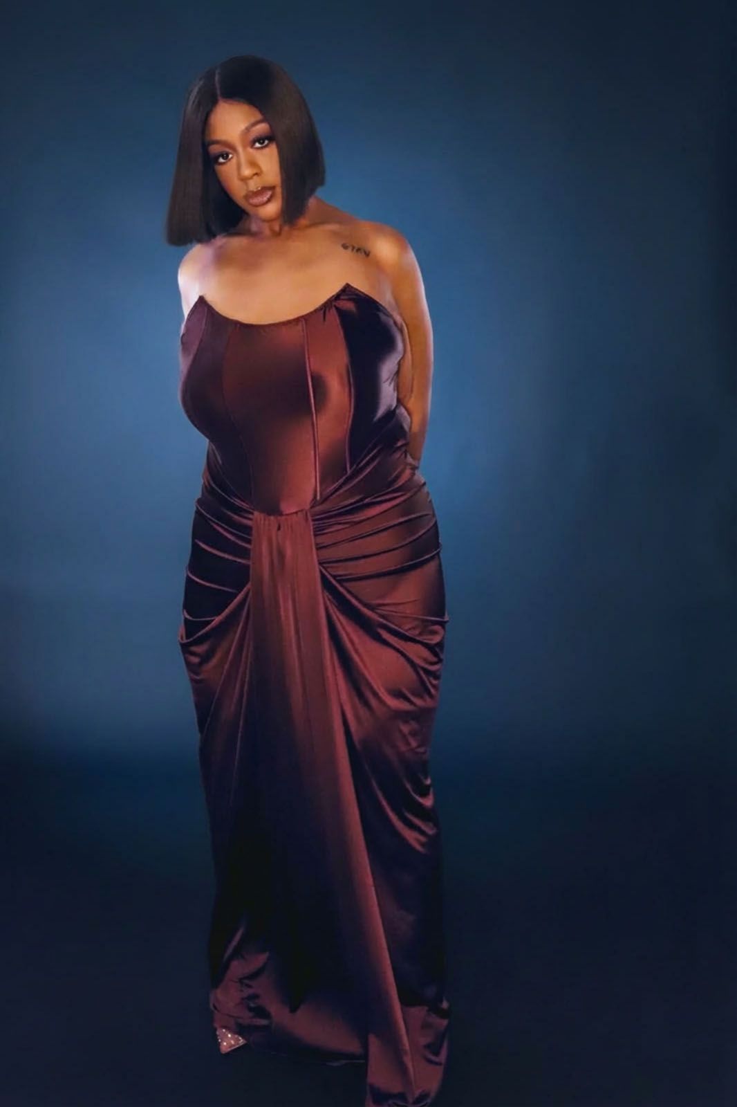A model poses in a luxurious burgundy velvet dress against a dark blue backdrop in a fashion photoshoot series.