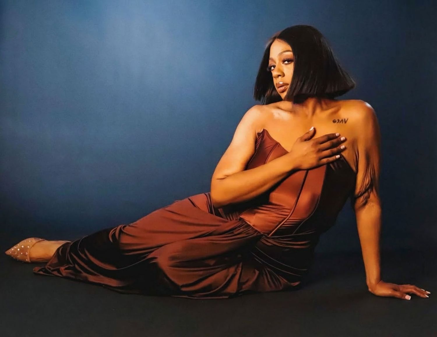 A figure in a flowing burgundy dress poses gracefully against a dark blue background in a series of artistic portraits.