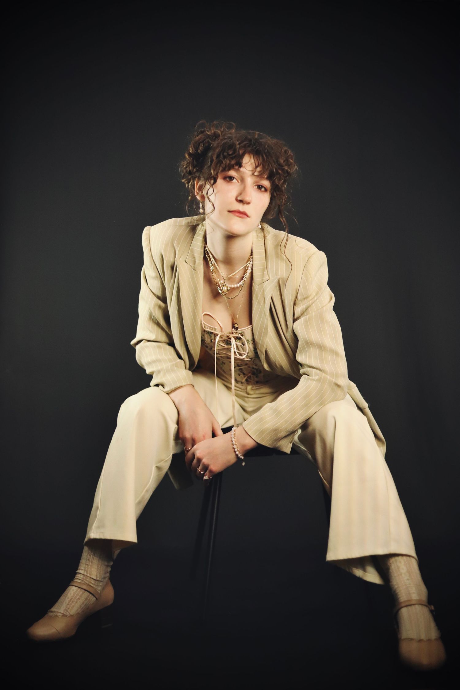 A figure in a beige suit jacket and boots poses against a dark background in a series of artistic fashion shots.