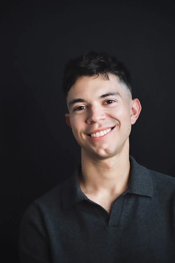 Casual portrait in dark polo showing warm smile against black backdrop.