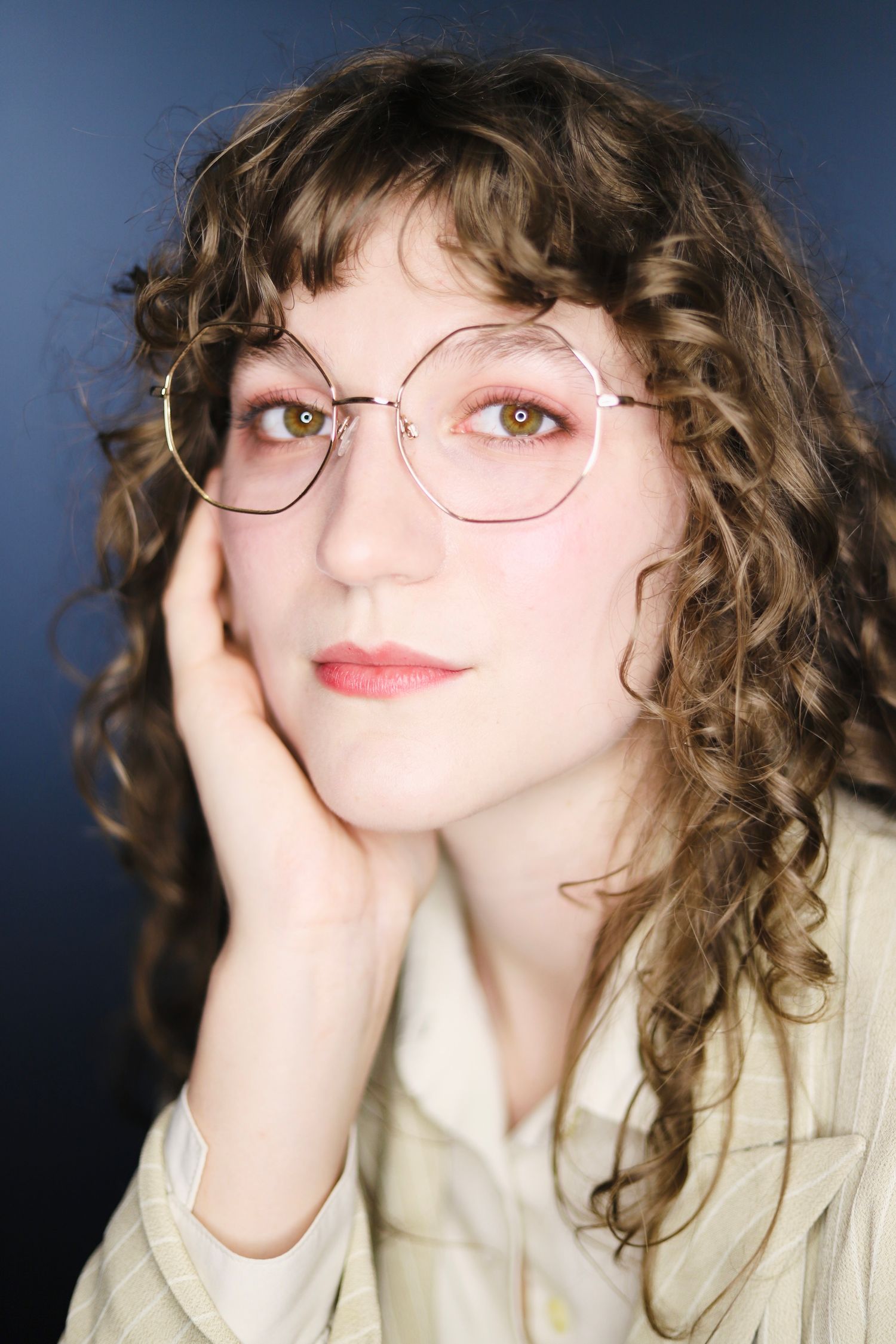 Artistic headshots featuring whimsical poses and round glasses against dark backdrop.