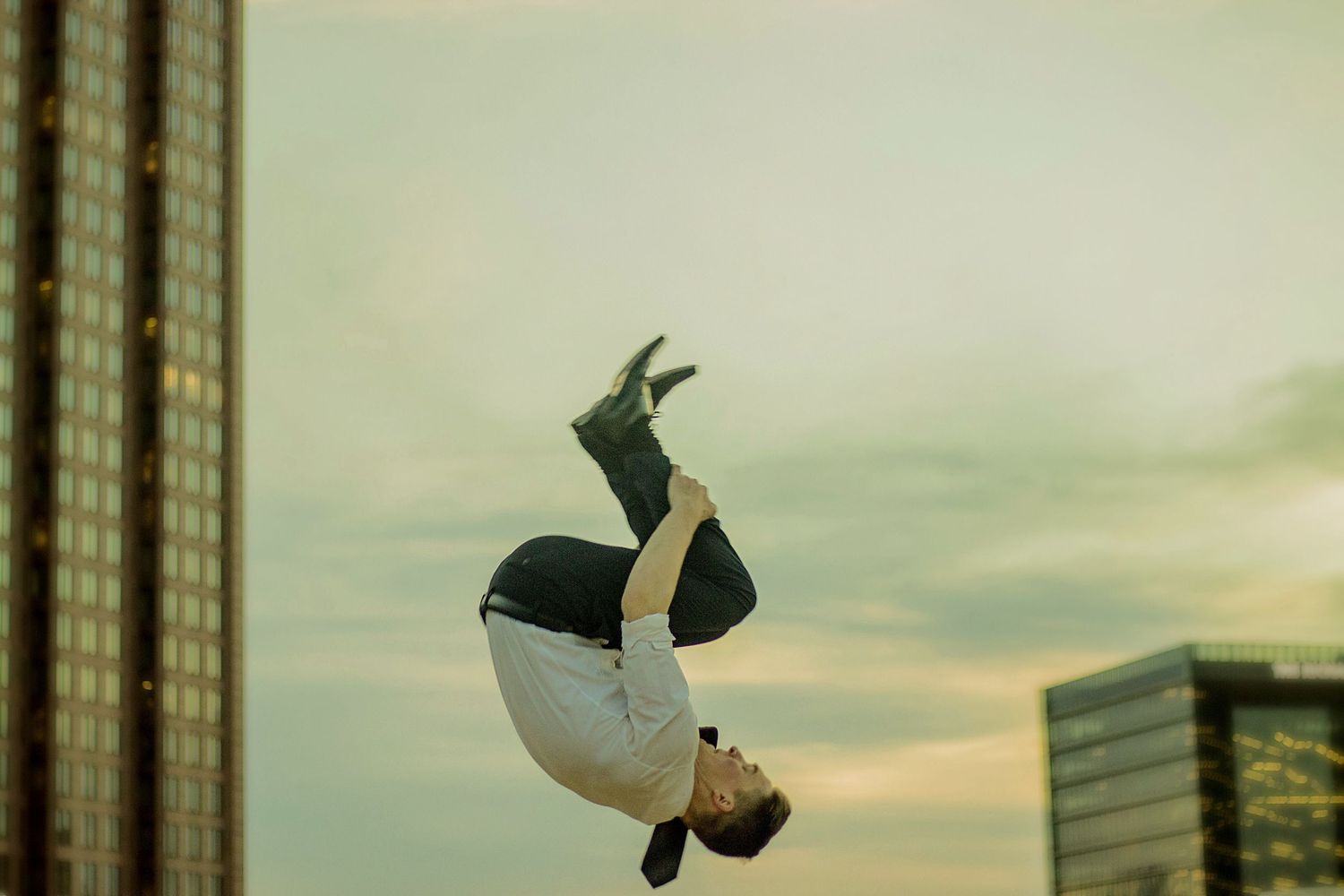 Person performing acrobatic flip against city building backdrop.