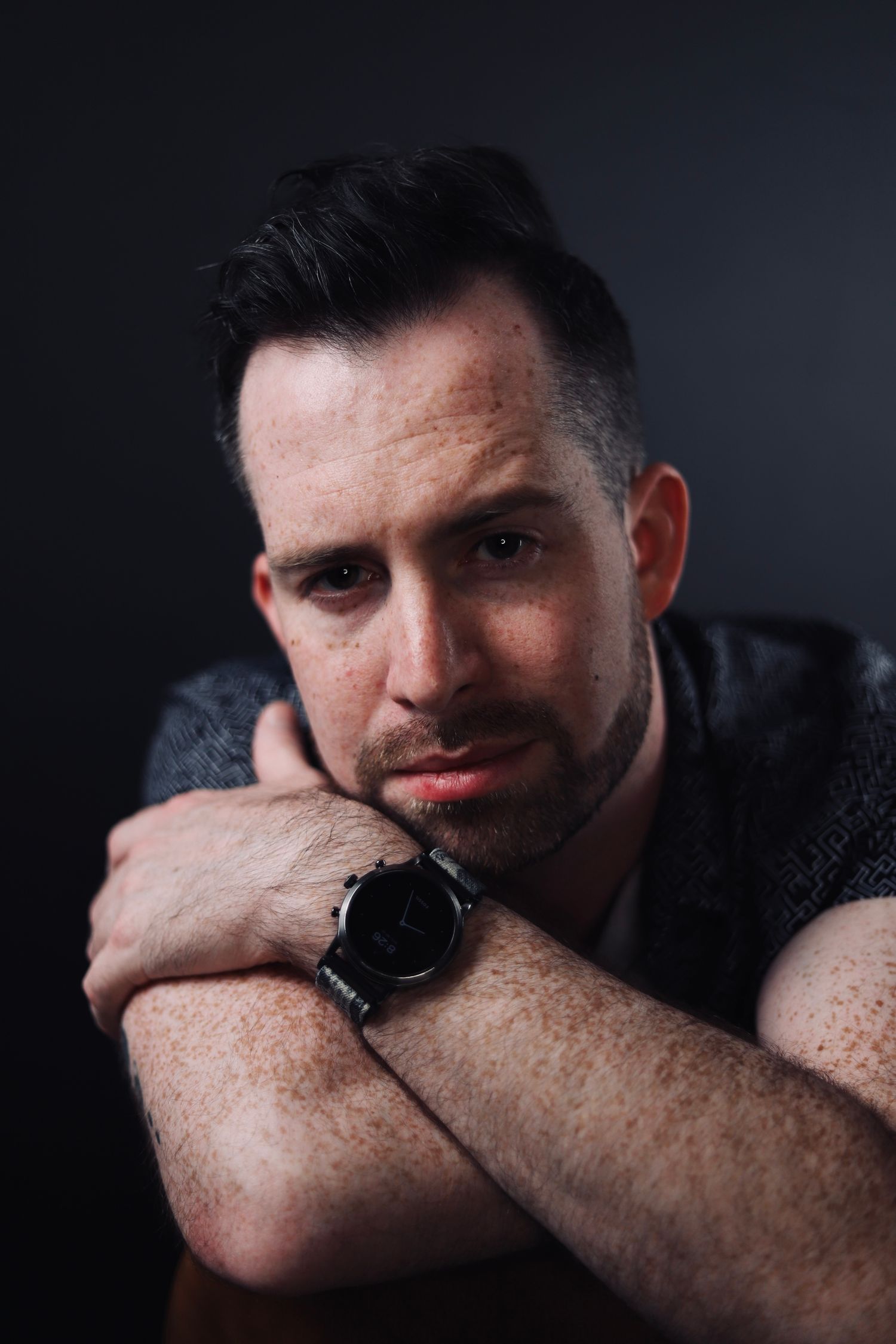 Dramatic studio portrait showing a dark watch and thoughtful expression in low key lighting.