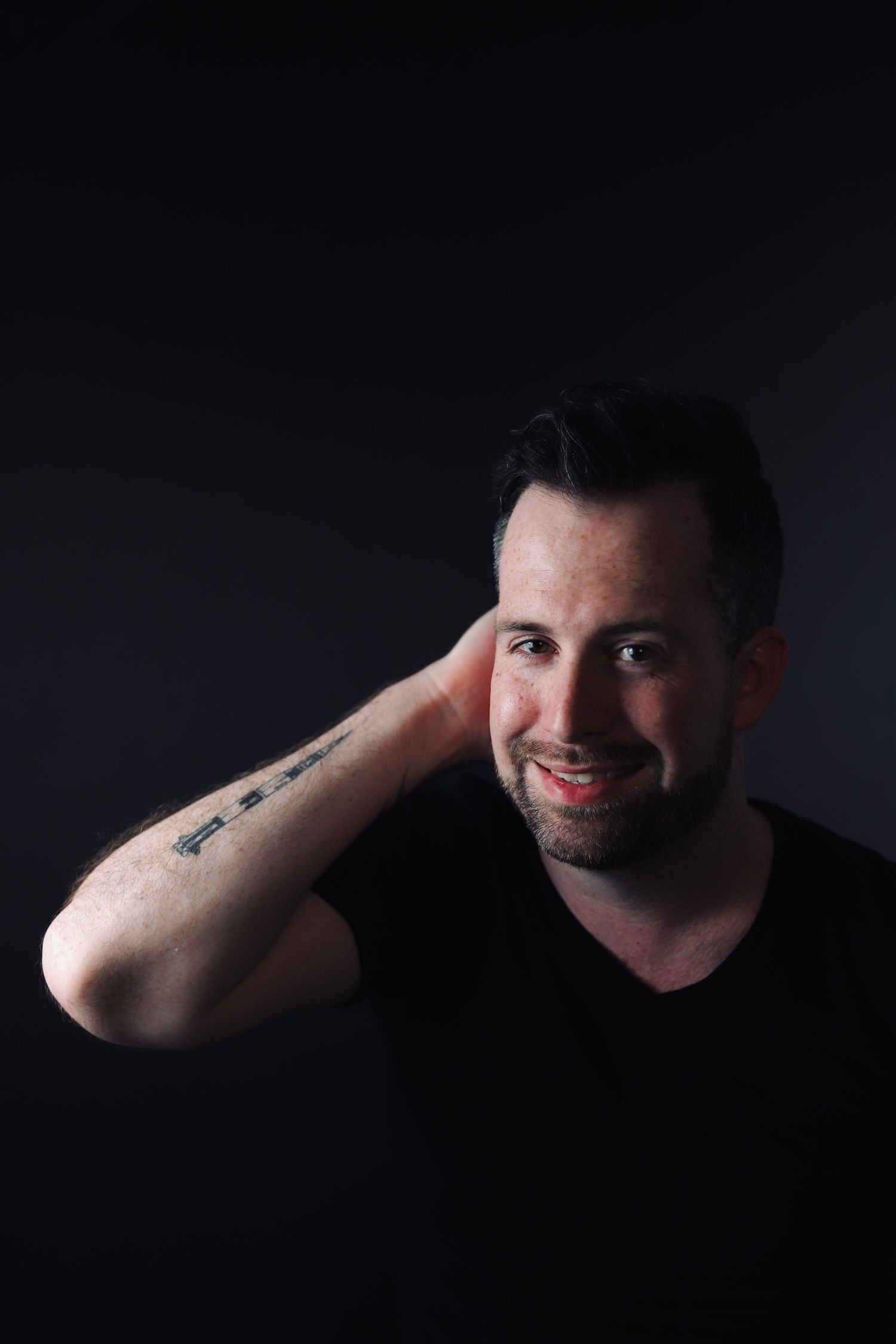Portrait of a person in black shirt showing arm tattoo with natural smile.