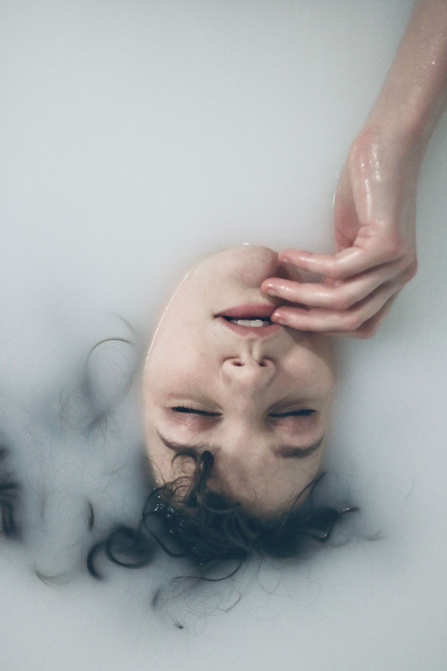 Artistic portrait of a person submerged in cloudy water with delicate hand placement.