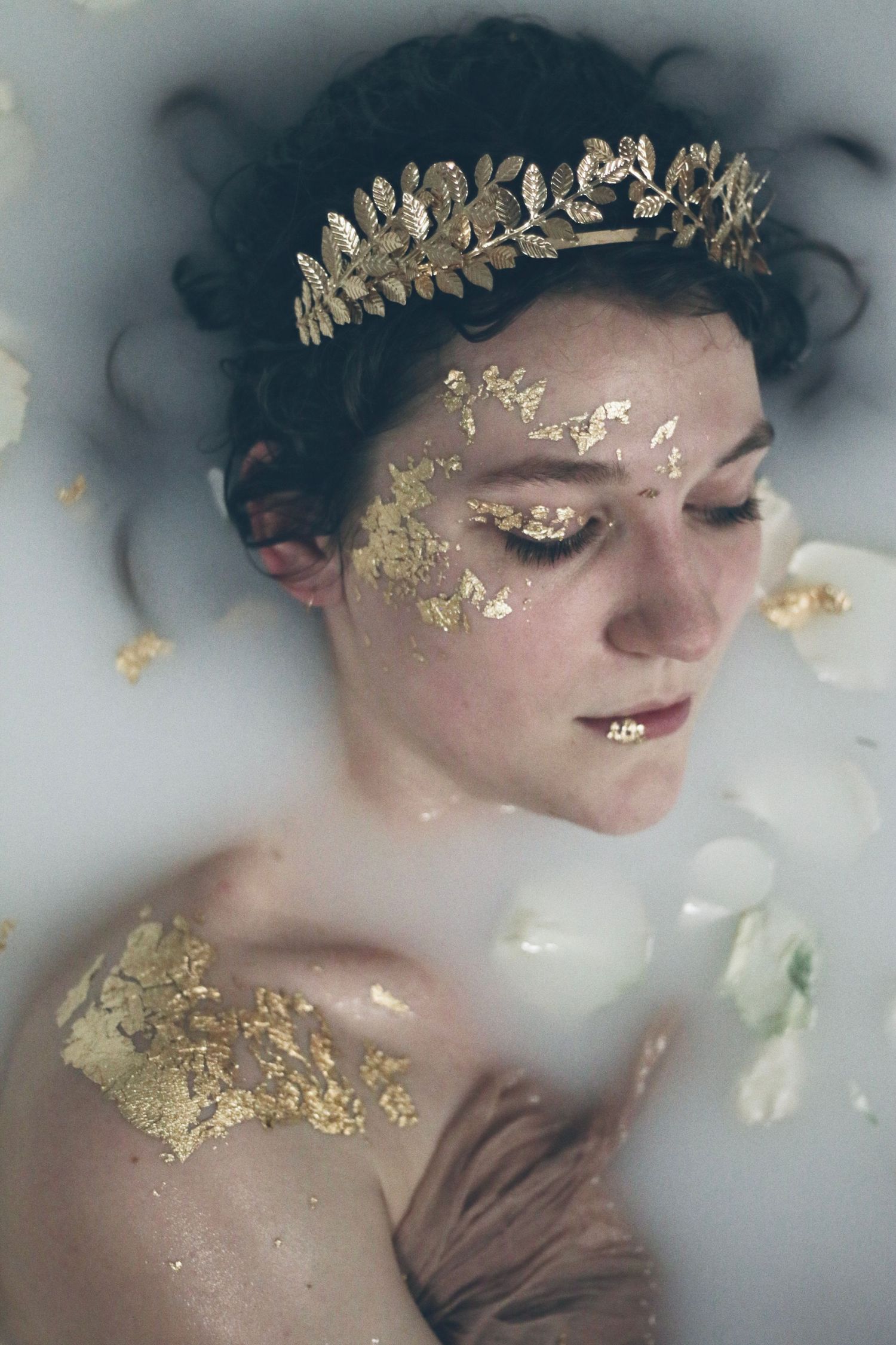 Ethereal portrait with gold leaf accents and metallic crown in milky water.