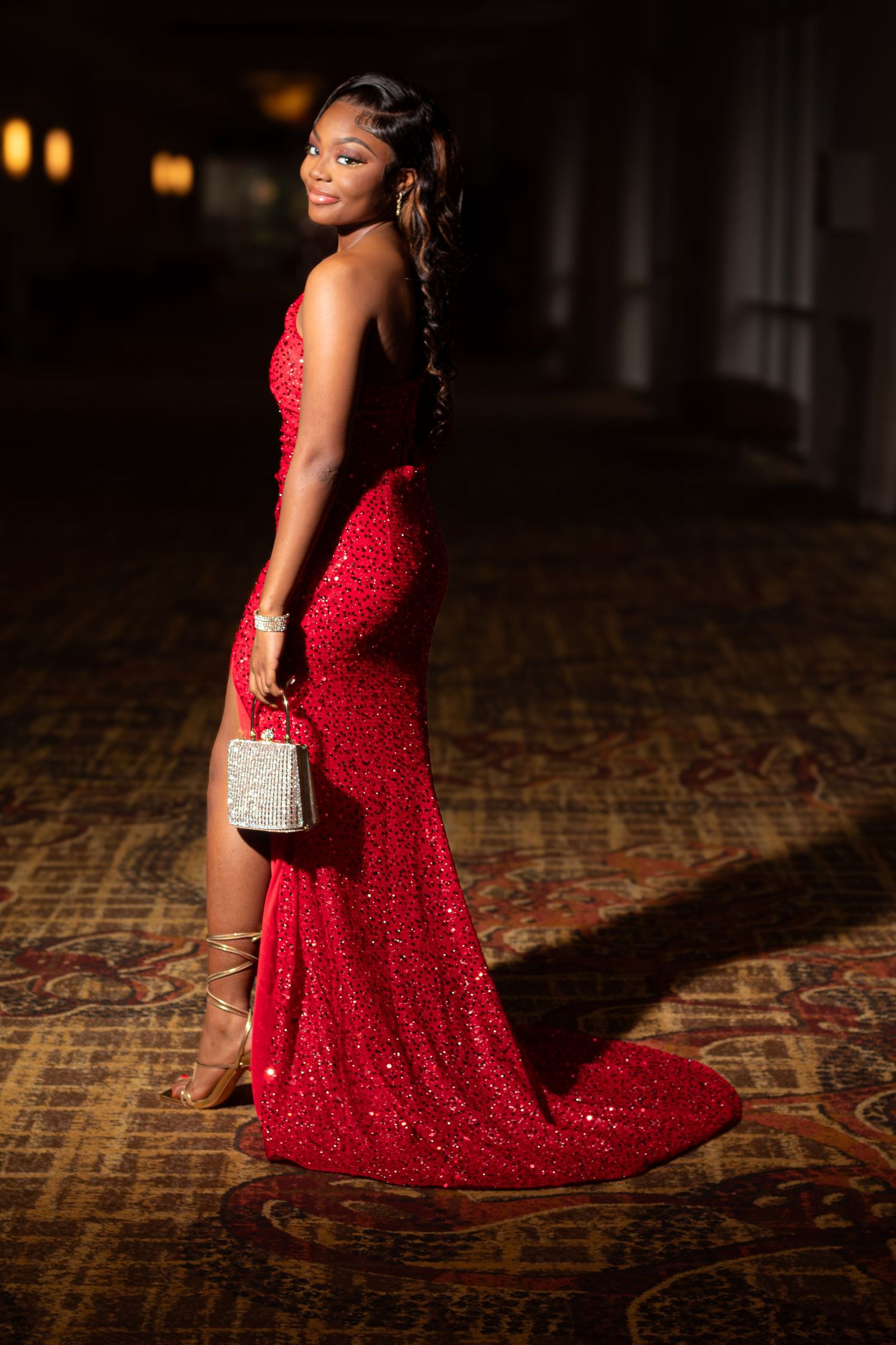 Young woman in a sparkling red sequin gown holding a crystal clutch, posing elegantly at a formal event.