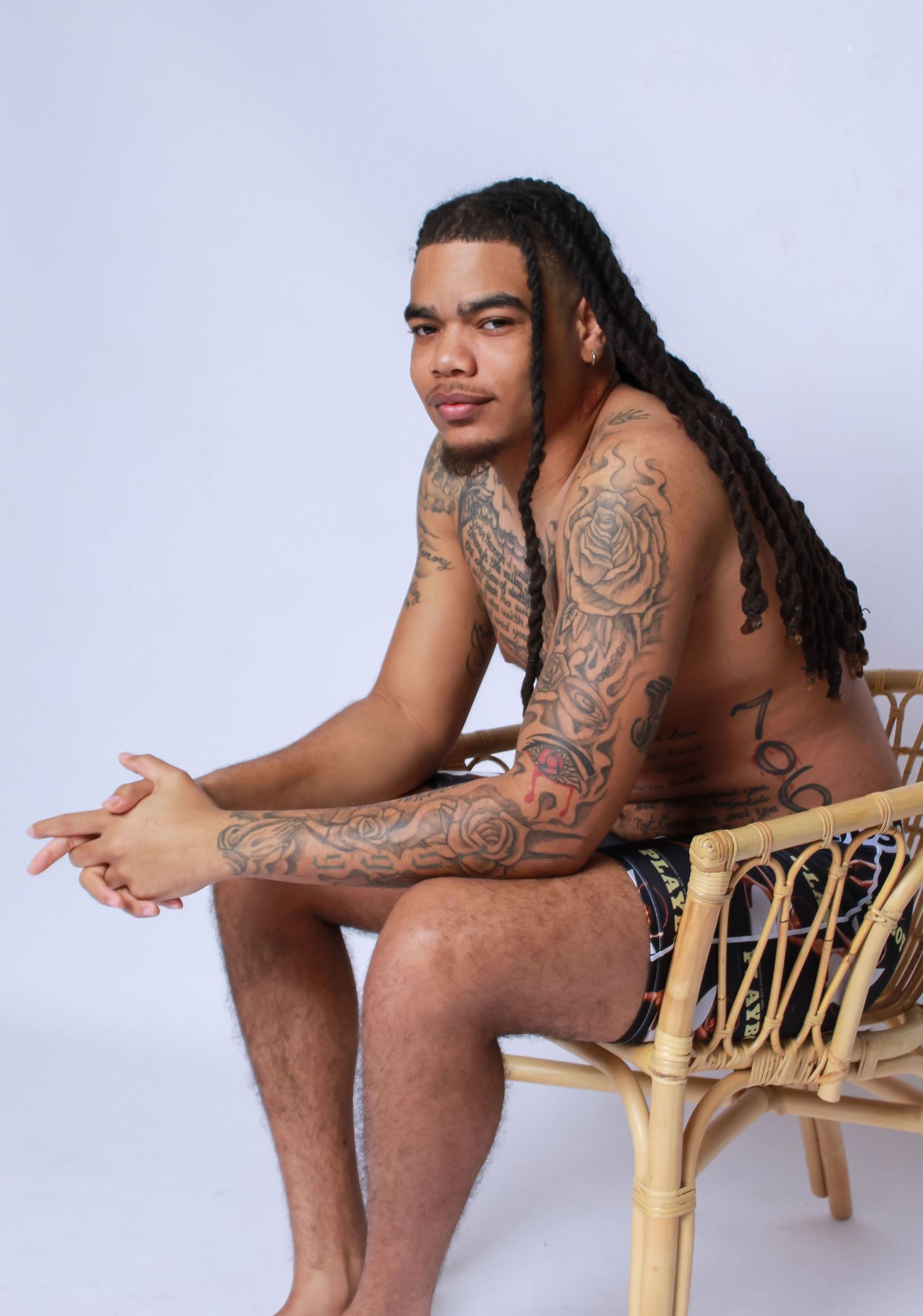 Studio modeling portrait of a man seated confidently, highlighting form, tattoos, and natural expression
