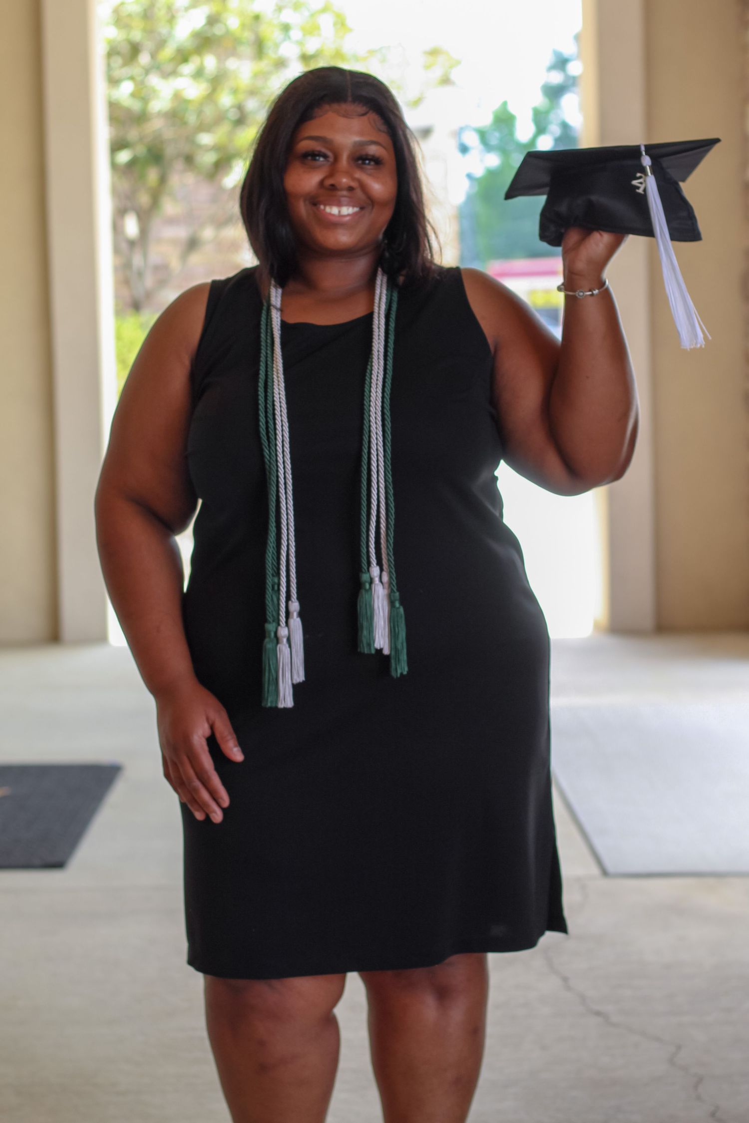 Graduate smiling while holding a graduation cap during an indoor milestone portrait session captured by PctrMe Photography