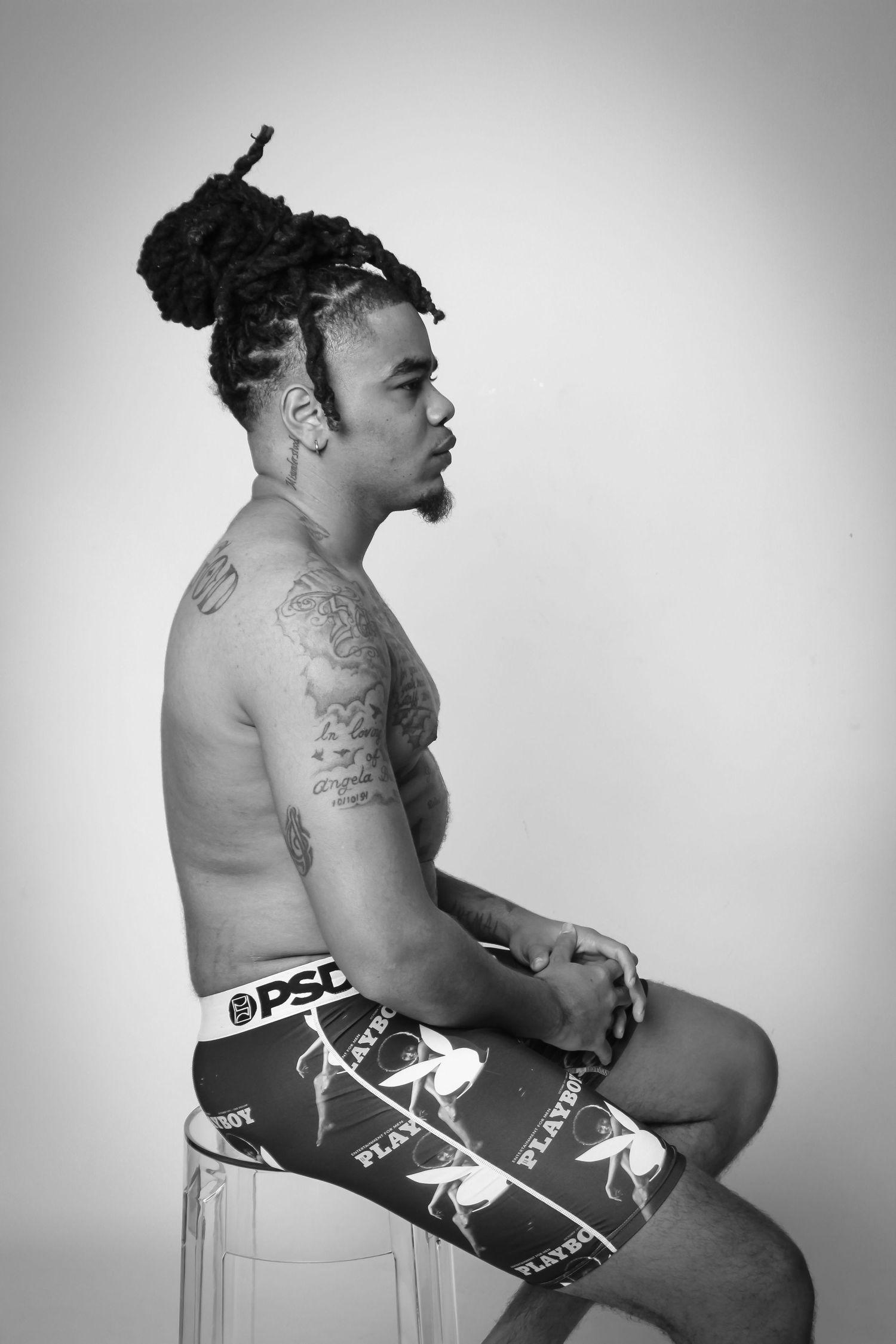 Black and white editorial portrait of a male model seated in profile, highlighting strength, form, and expression
