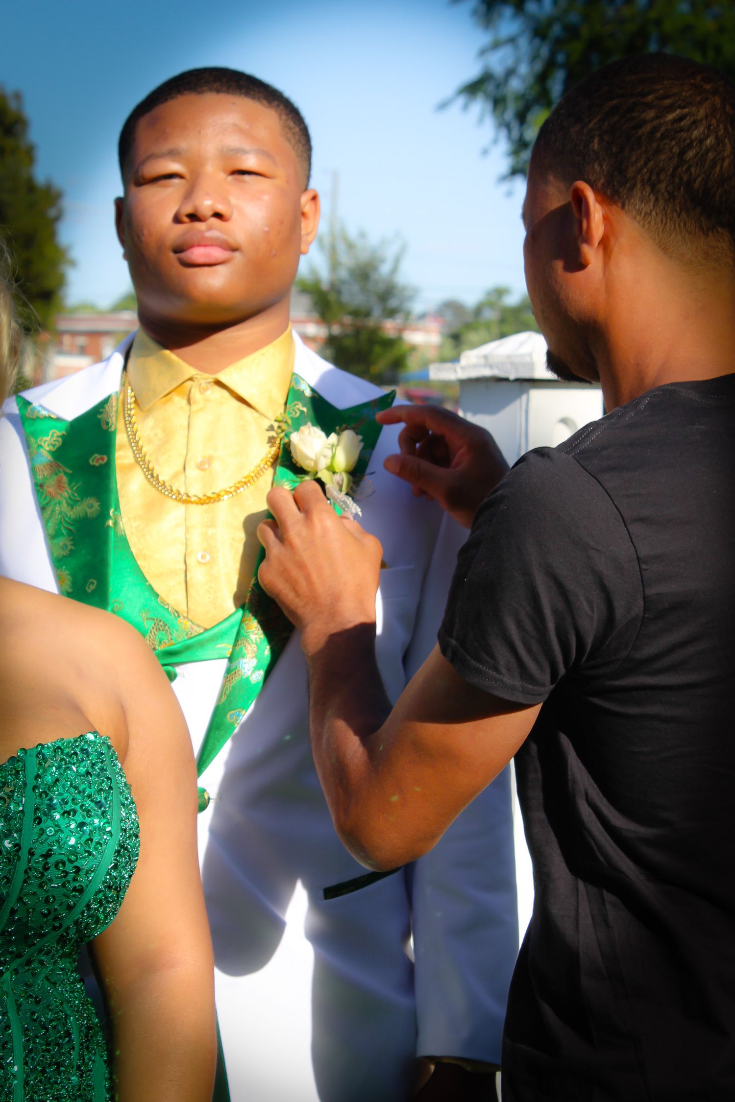 Candid moment of a young man having his boutonniere adjusted before a formal event or milestone celebration