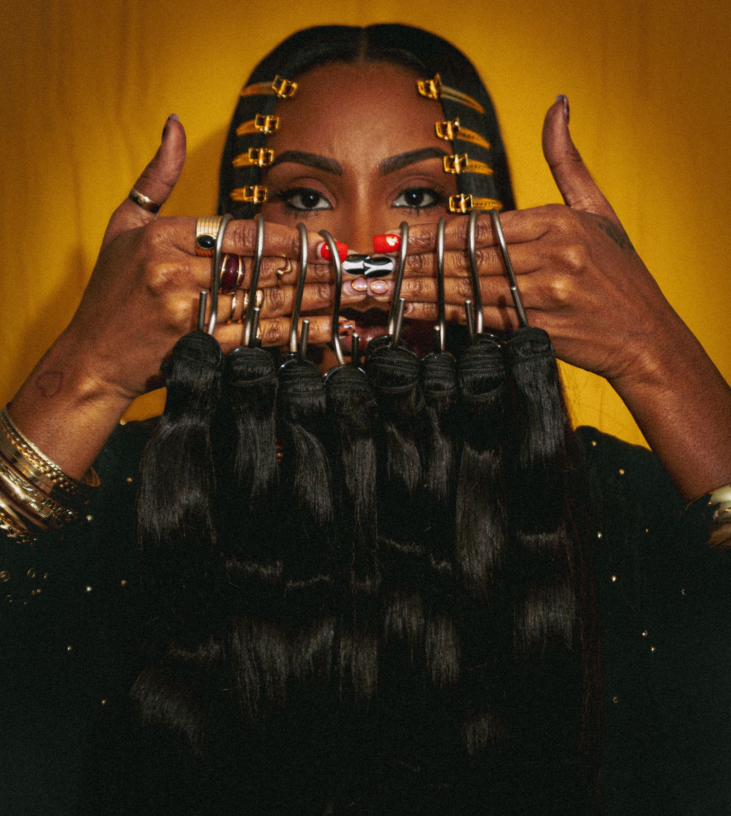 Person wearing gold rings holds their hands up to their face against a golden background with dramatic lighting.