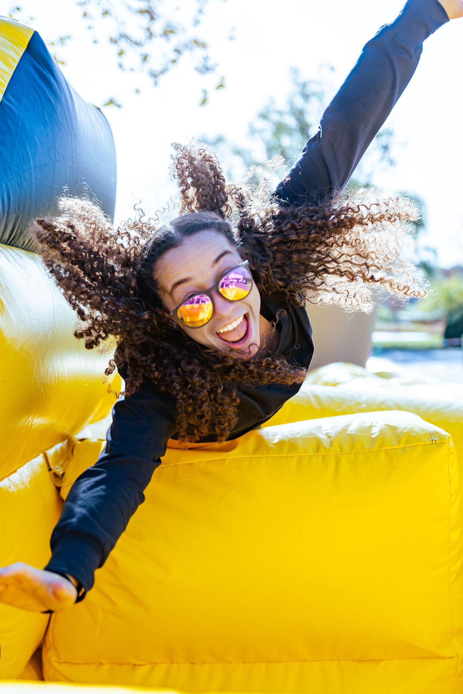 Person with curly hair lying on yellow surface making playful poses.
