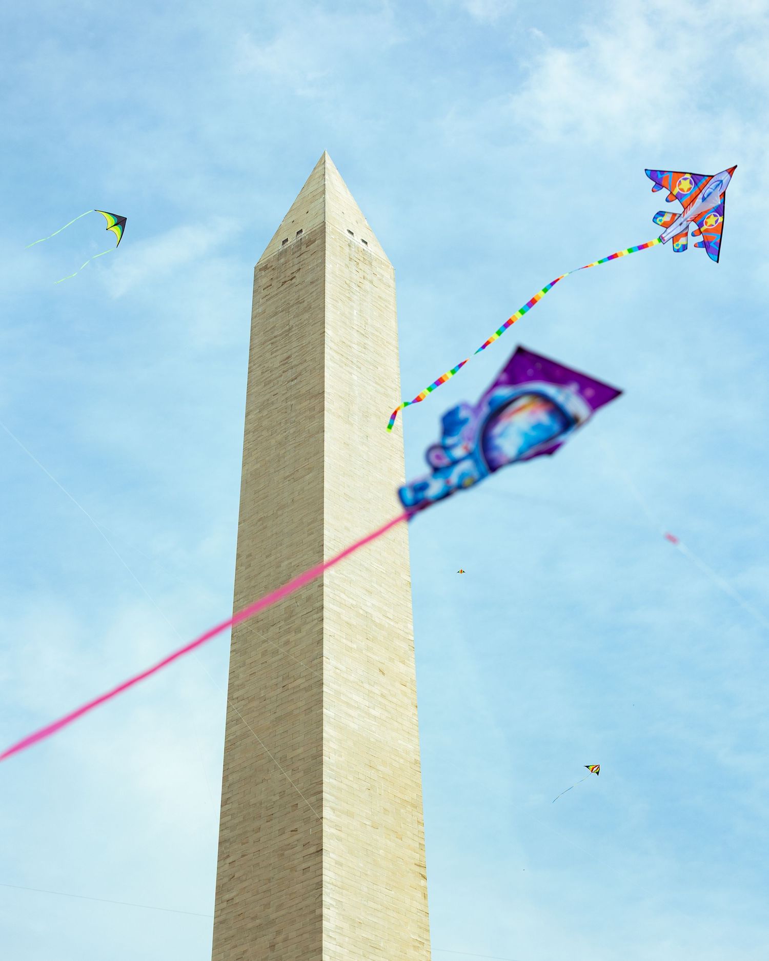 Multiple kites flying in front of the Washington Monument on a sunny day.
