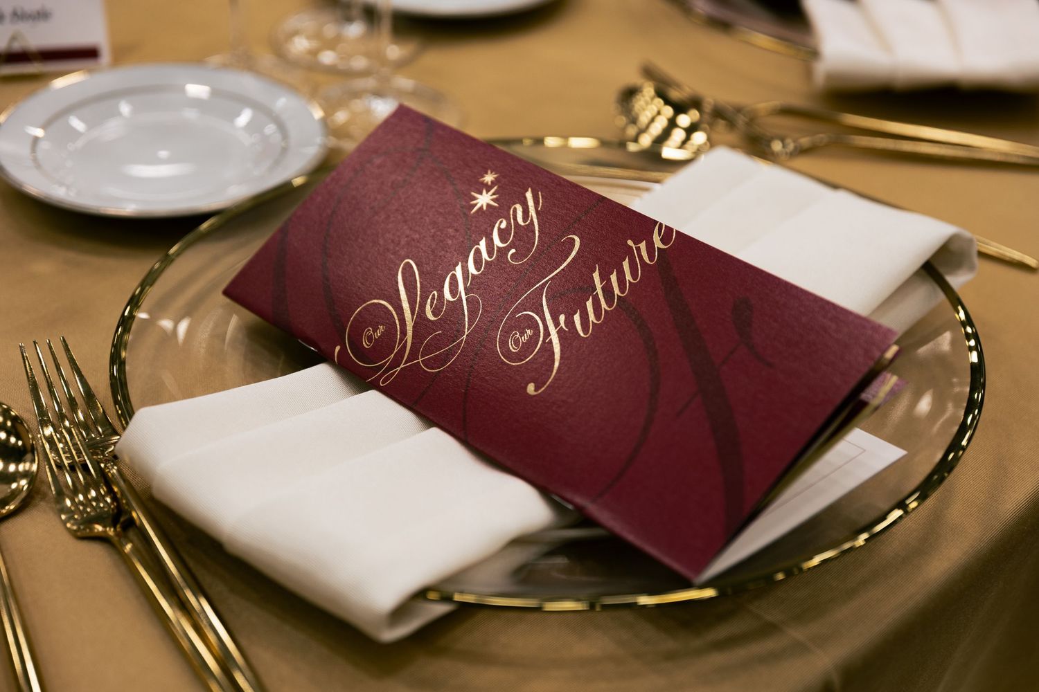 Elegant place setting with burgundy menu card and white napkin on gold-rimmed plate.