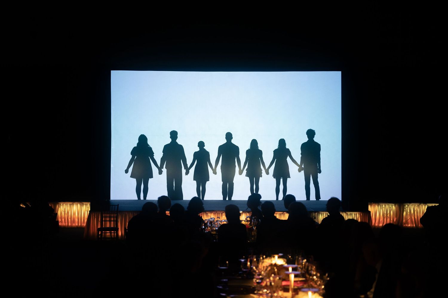 Silhouettes of people standing against a bright background with dramatic lighting.