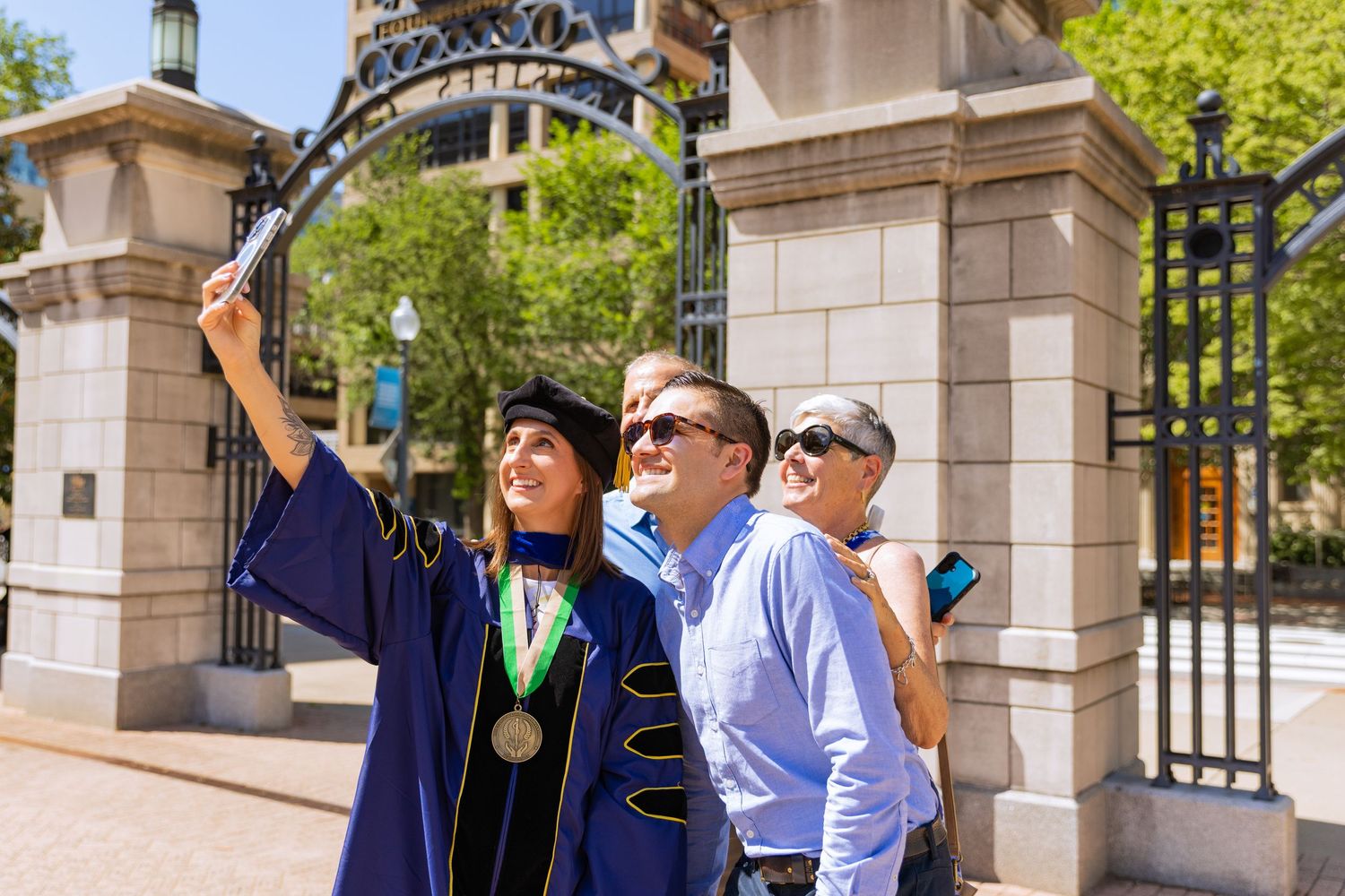 A group of people in graduation attire walk through stone archways on a sunny day during commencement ceremonies.