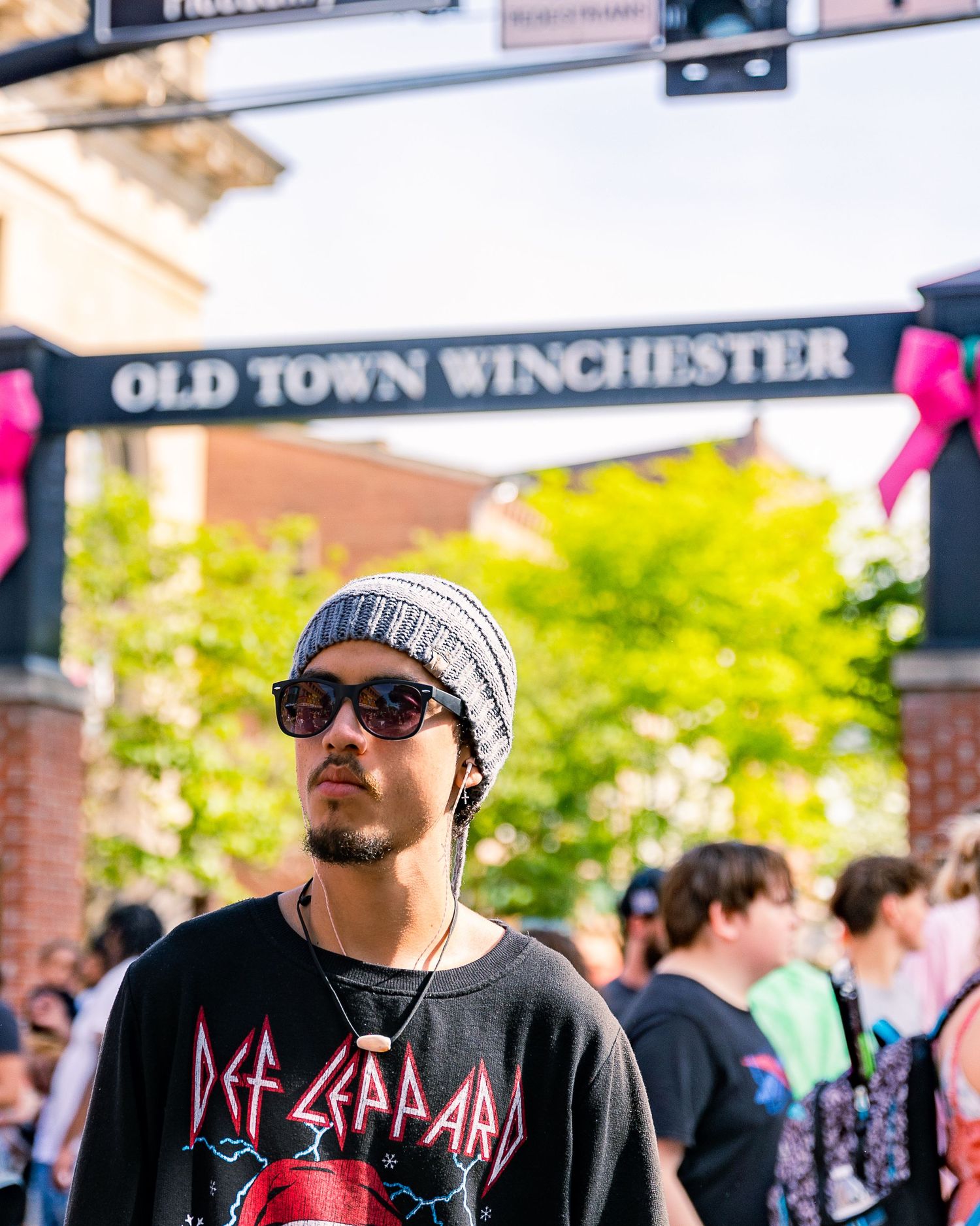 Man in Def Leppard shirt and beanie at Old Town Winchester outdoor event on a sunny day.