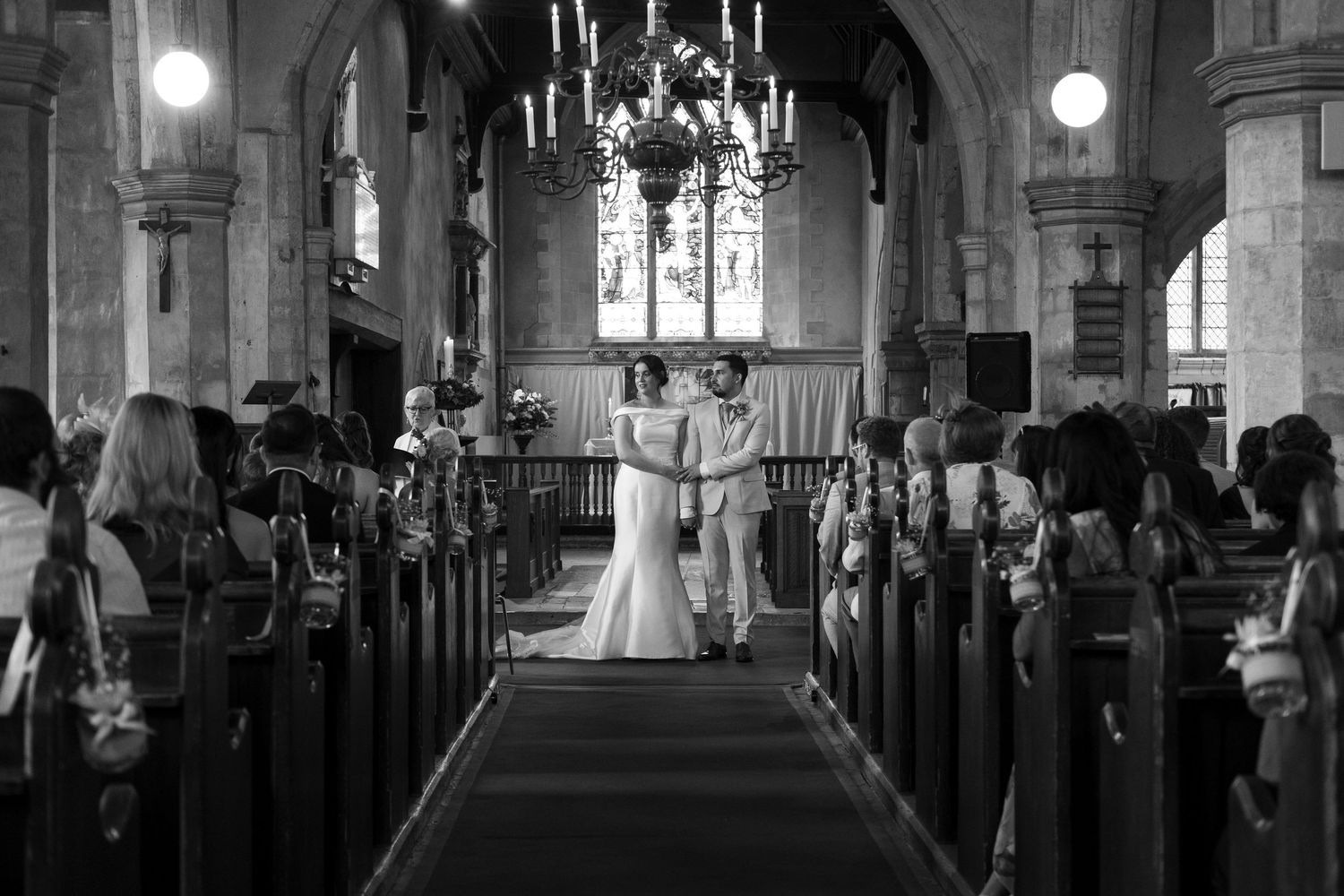 Wide angle view of a wedding ceremony in a historic church with vaulted ceilings and wooden pews.