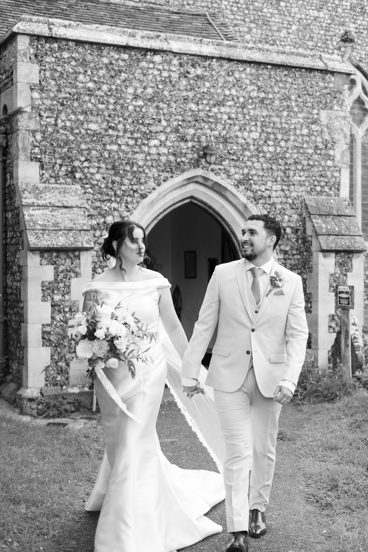 Black and white portrait of a couple outside a stone church entrance.