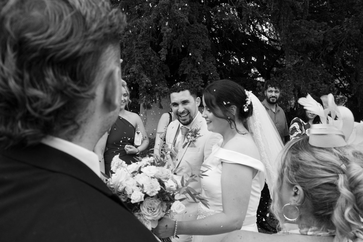 Black and white candid photo of wedding guests socializing outdoors.