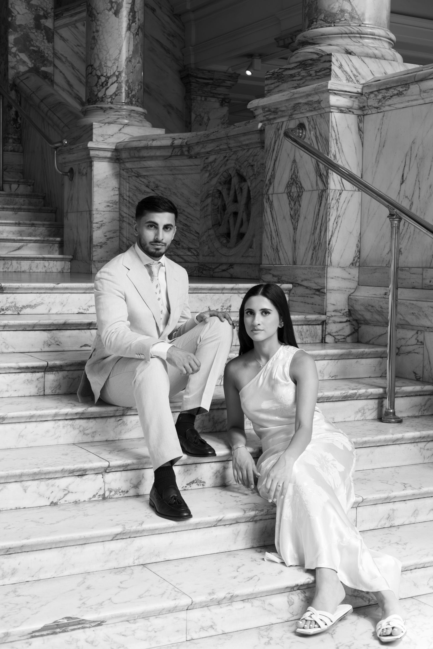 Wedding couple seated on marble steps in a grand historic building interior.