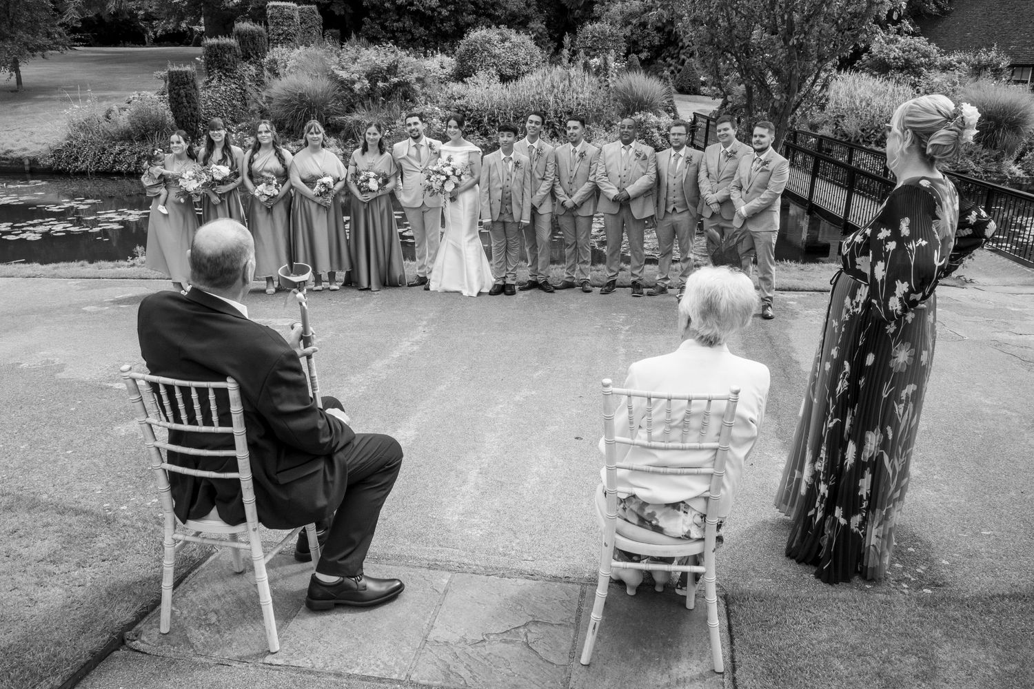 Wedding ceremony setup with white chairs and guests gathered outdoors.