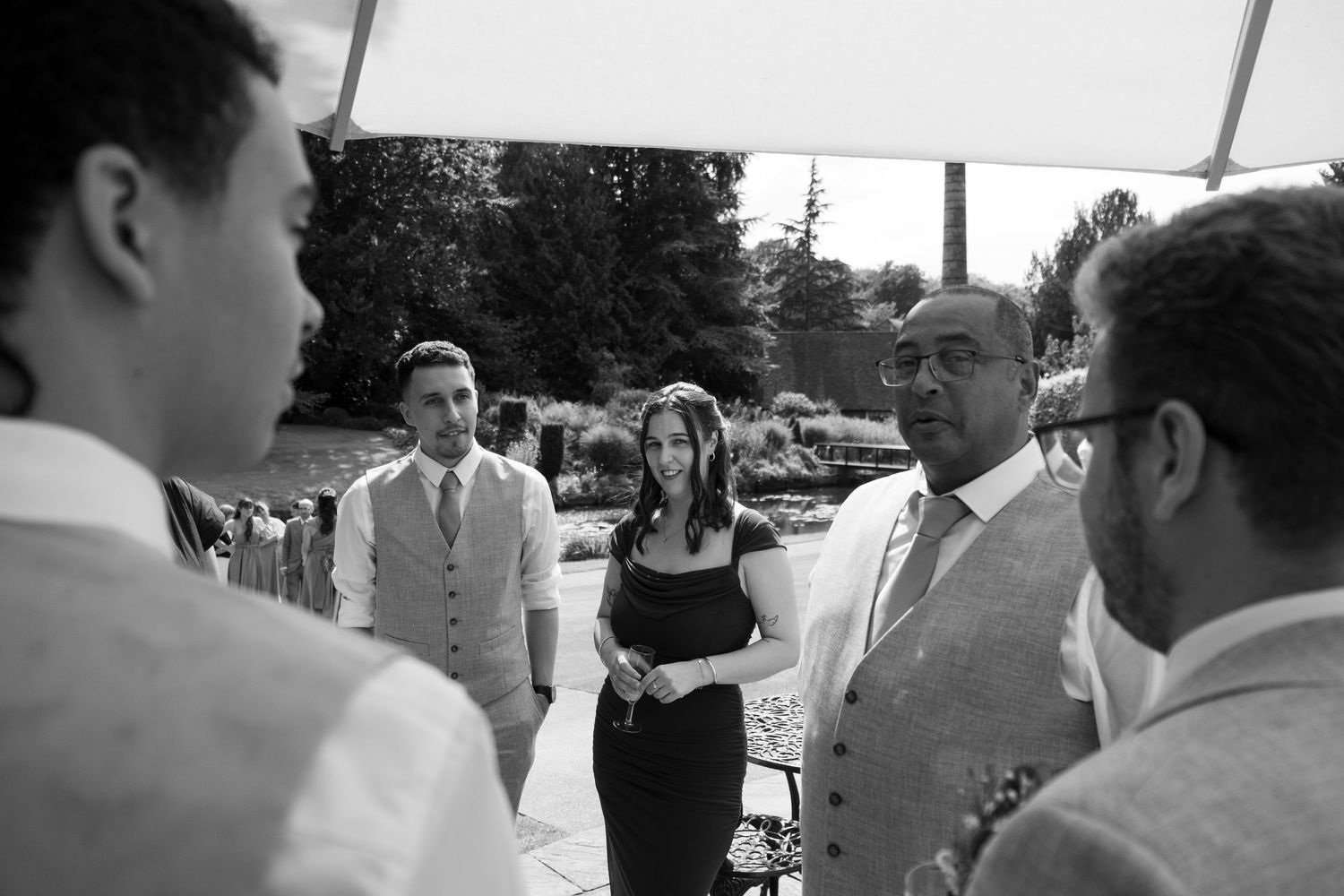 Black and white photo of wedding guests conversing under a white tent.
