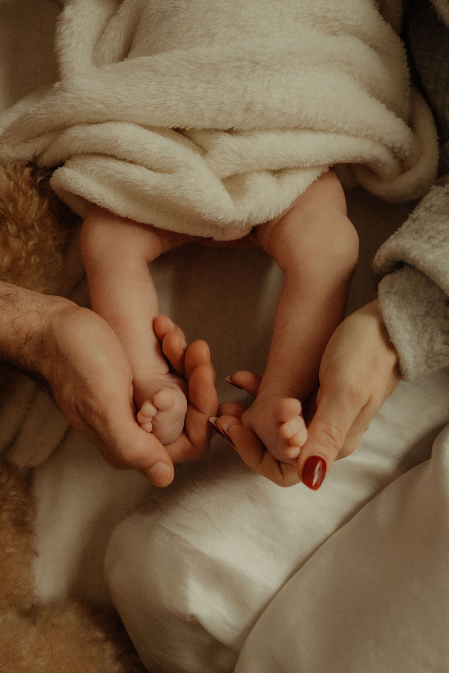 Close-up of hands gently holding tiny baby feet wrapped in soft blanket.