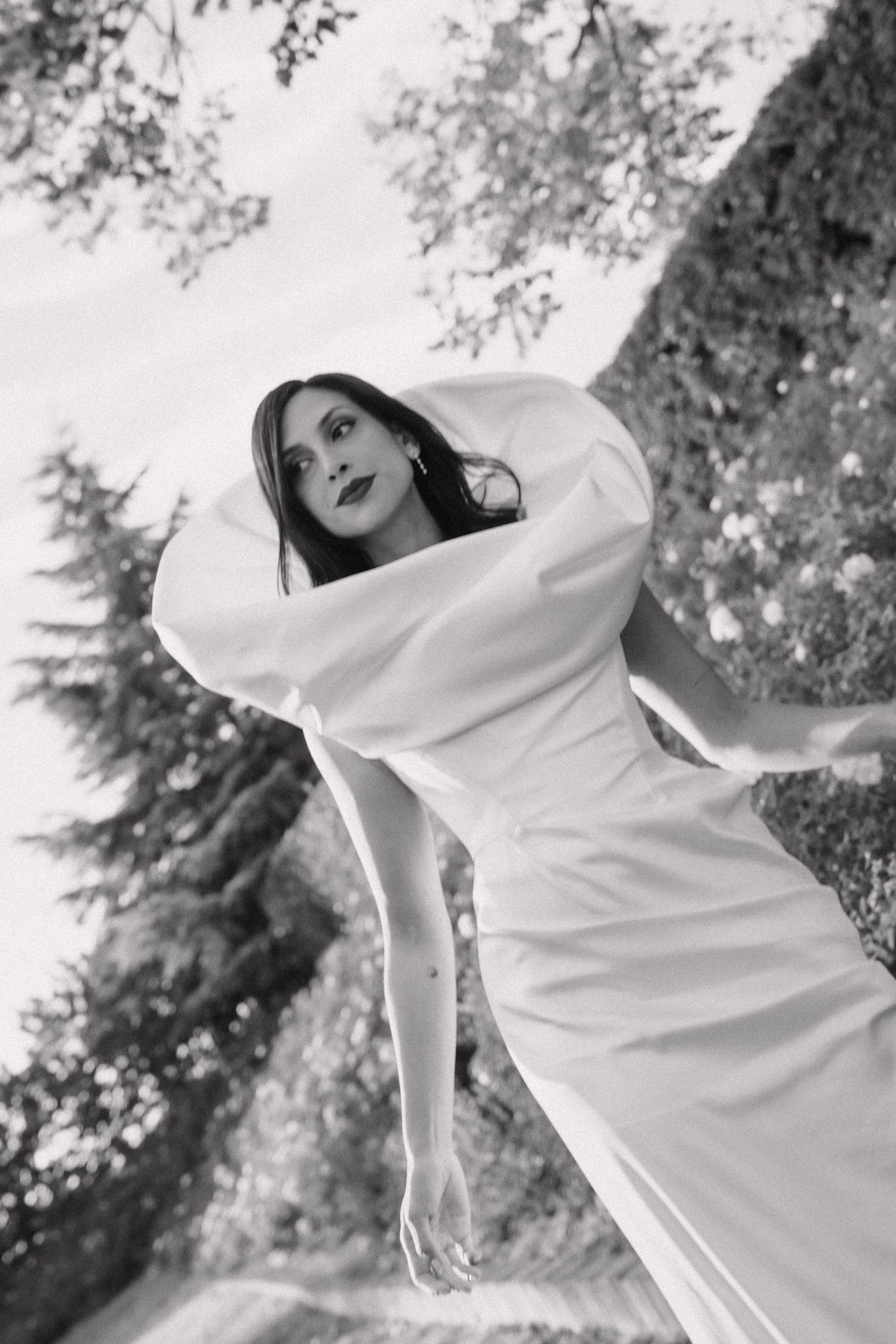 Artistic sequence of person in flowing white dress posing against trees in black and white.