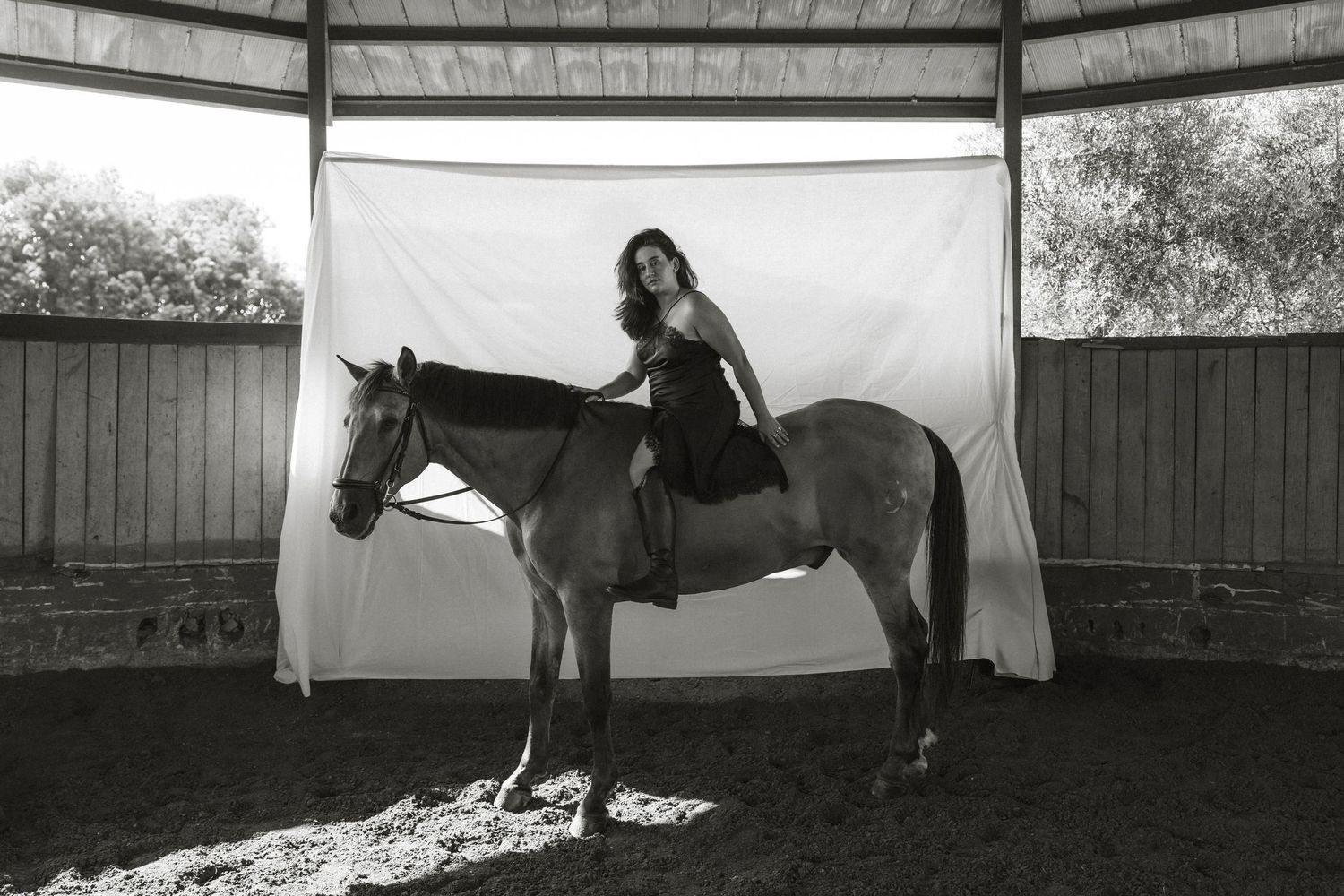 Artistic outdoor photoshoot with white sheets hanging on clothesline and horse in background.