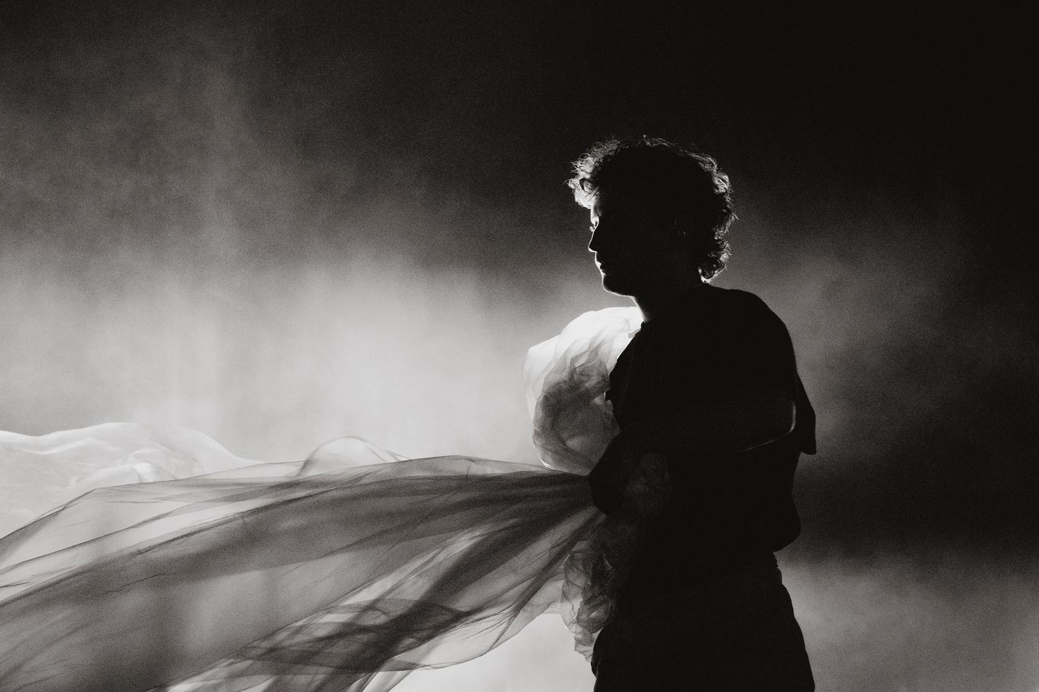 Dramatic silhouette of a figure with flowing fabric in dark atmospheric lighting.