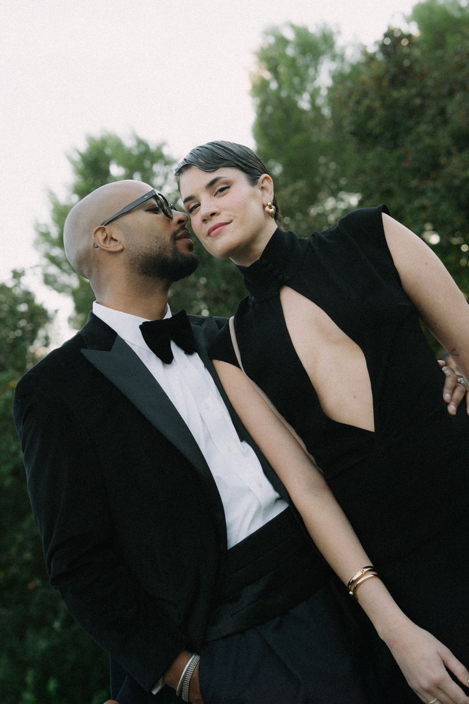 Elegant couple in formal black attire sharing intimate moments outdoors.
