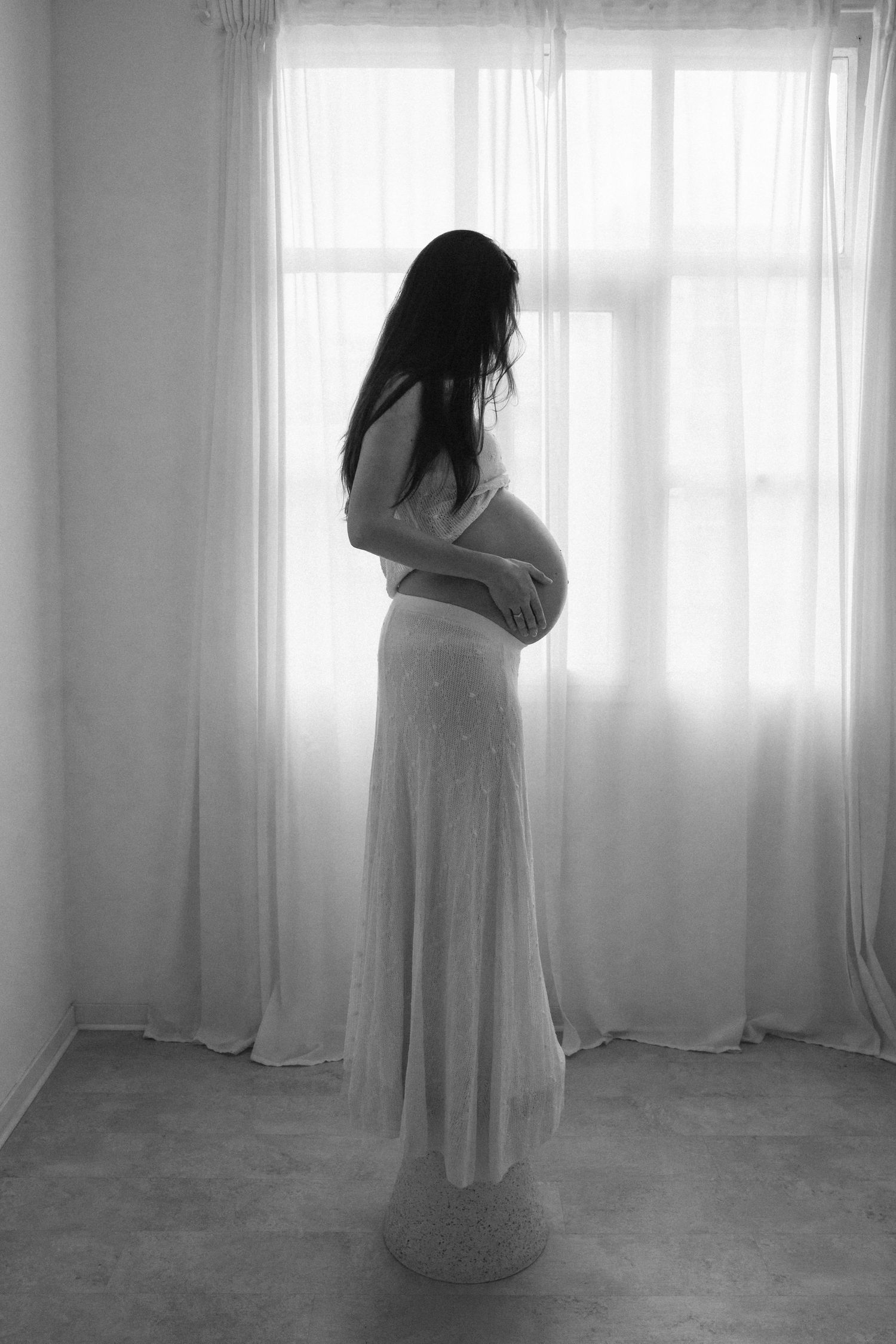 Minimalist photograph of a figure in white dress against bright windows.