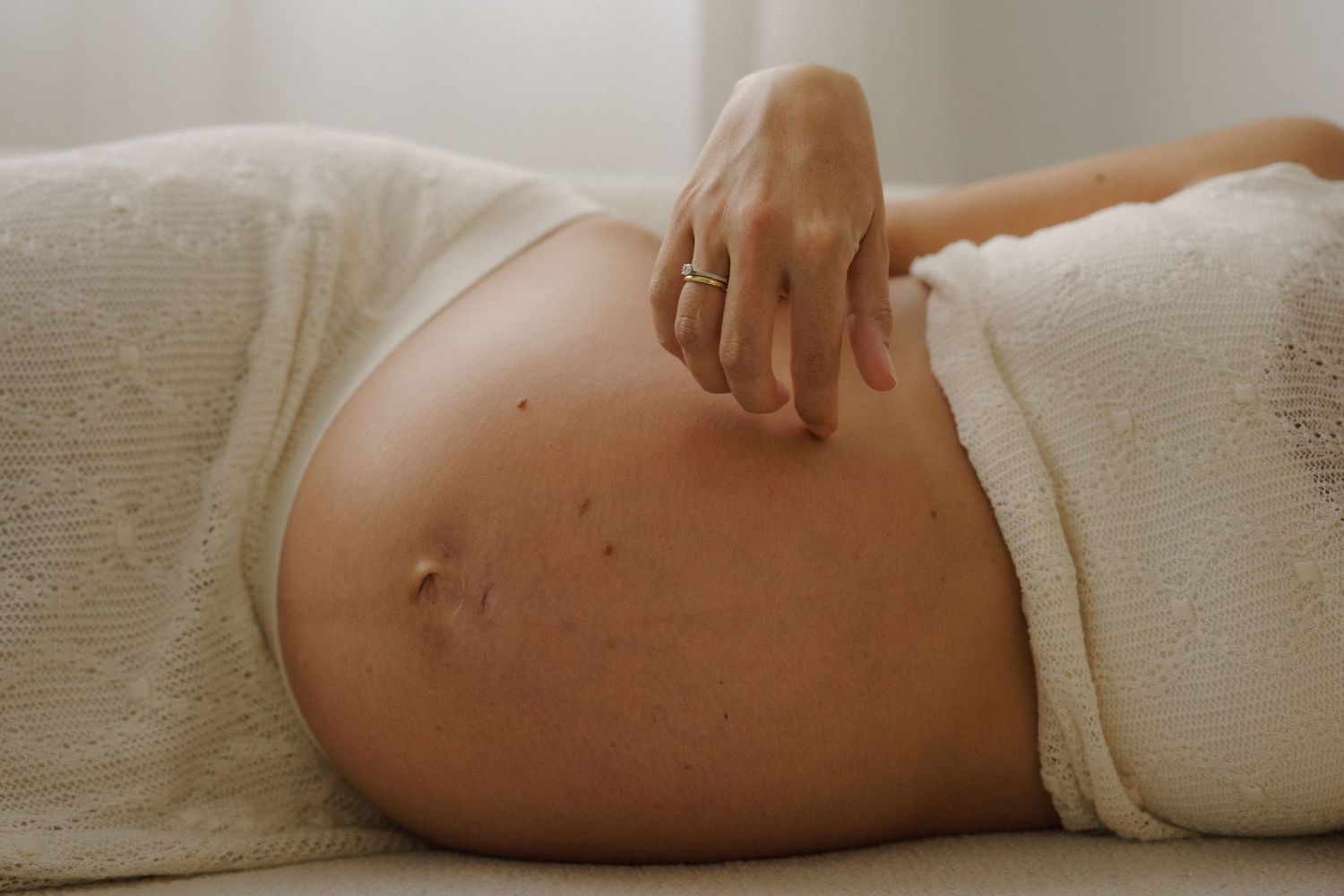 Close-up photos of pregnant belly wrapped in white fabric with gentle hands.