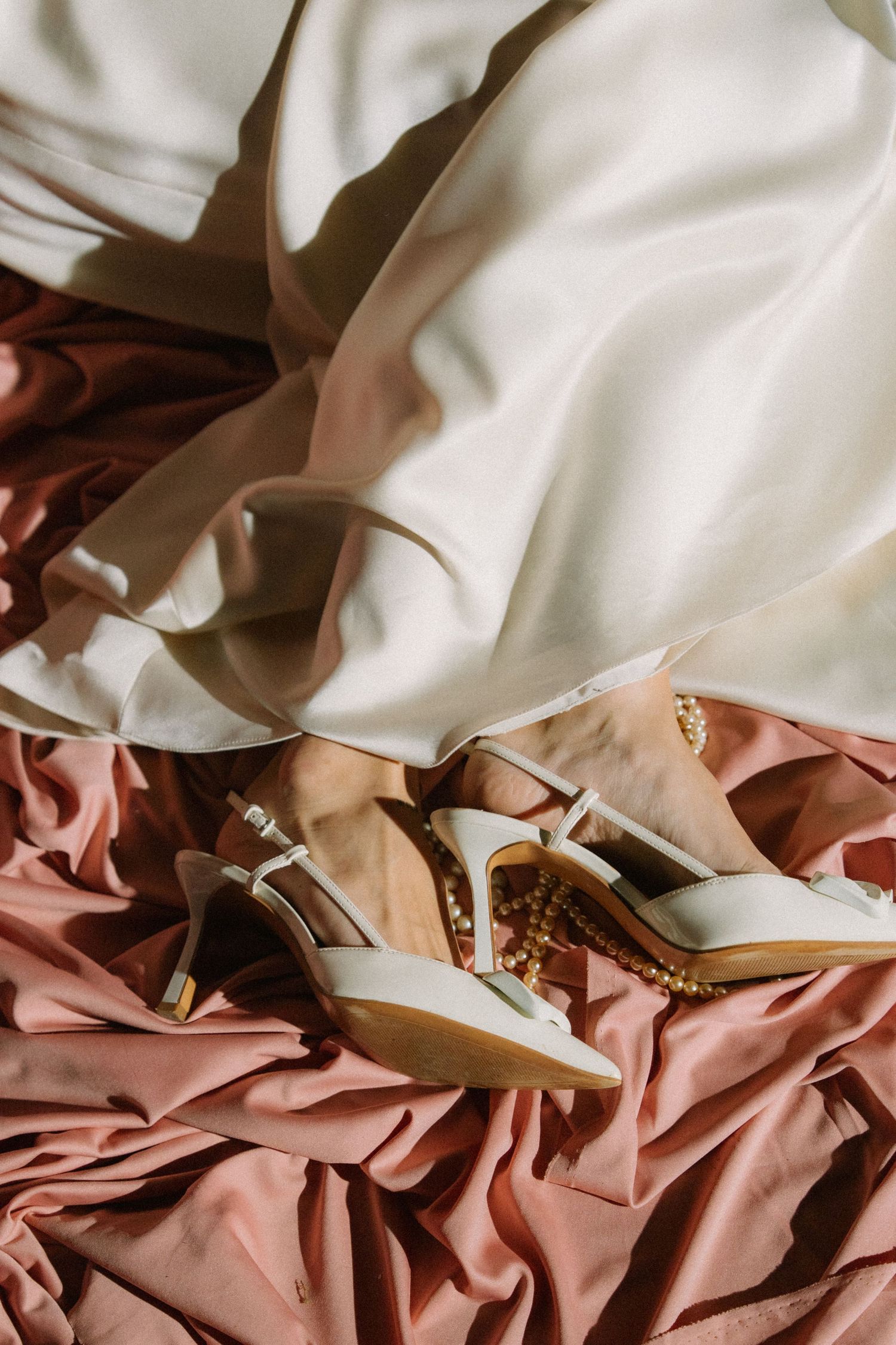 Close-up detail of white wedding dress fabric draped over dusty rose colored material.